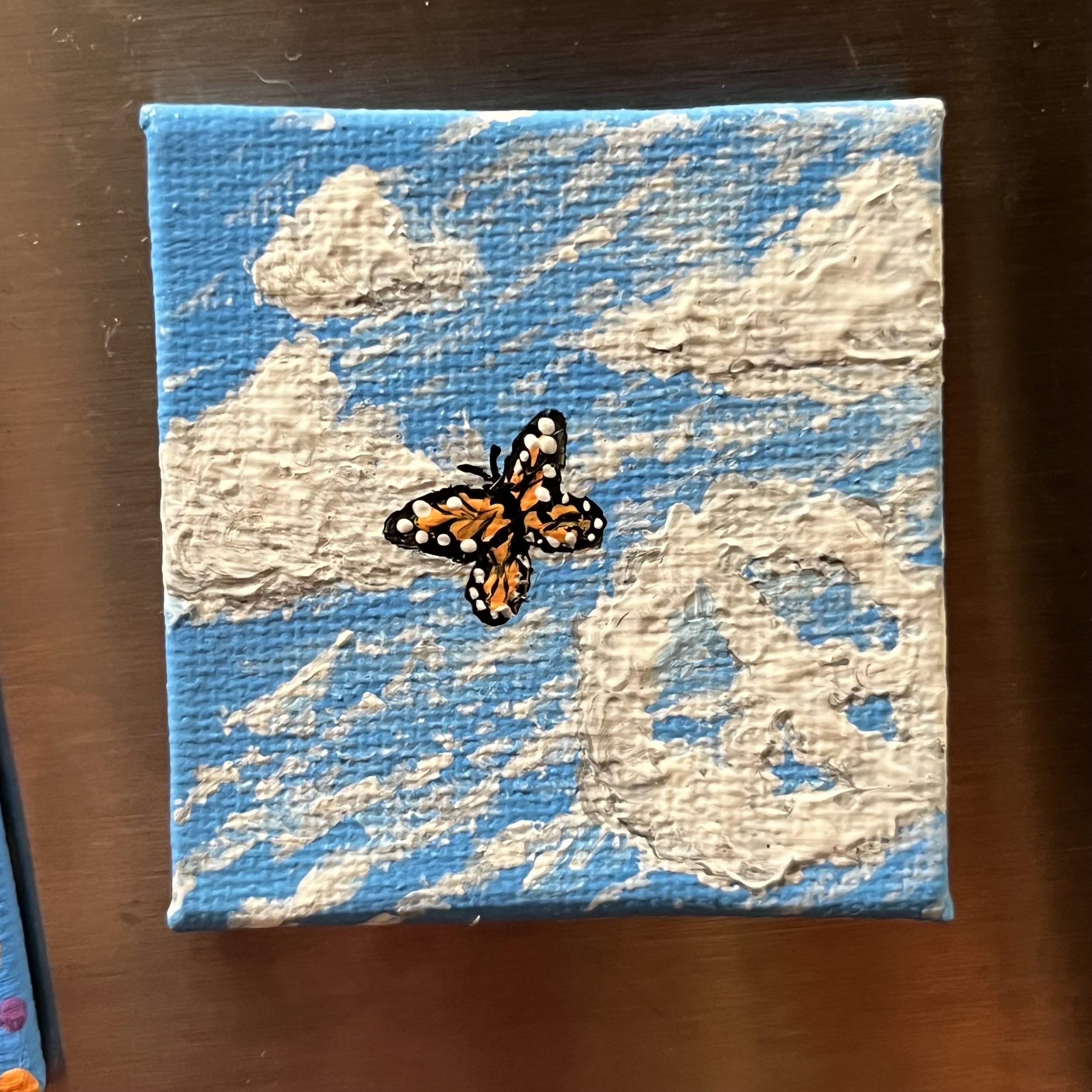Monarch butterfly in a blue sky with clouds, one cloud is a peace sign