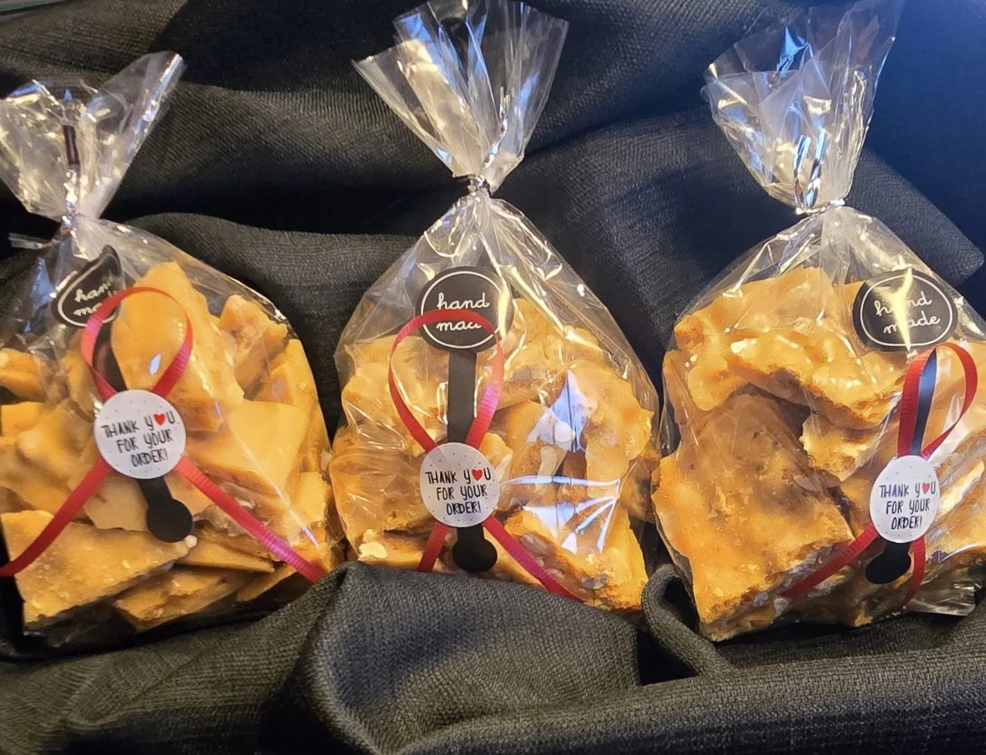 A packaged peanut brittle candy in clear plastic with black polka dots, labeled 'Peanut Brittle,' resting on black fabric.