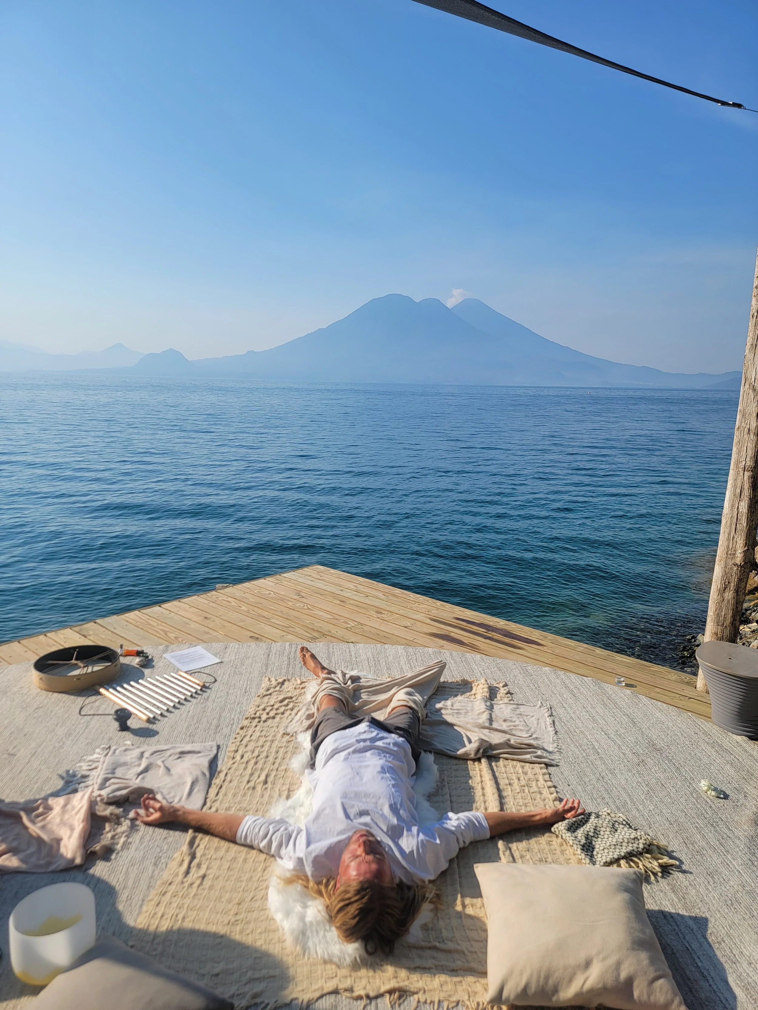 Person relaxing on a mat by the water with mountains in the background