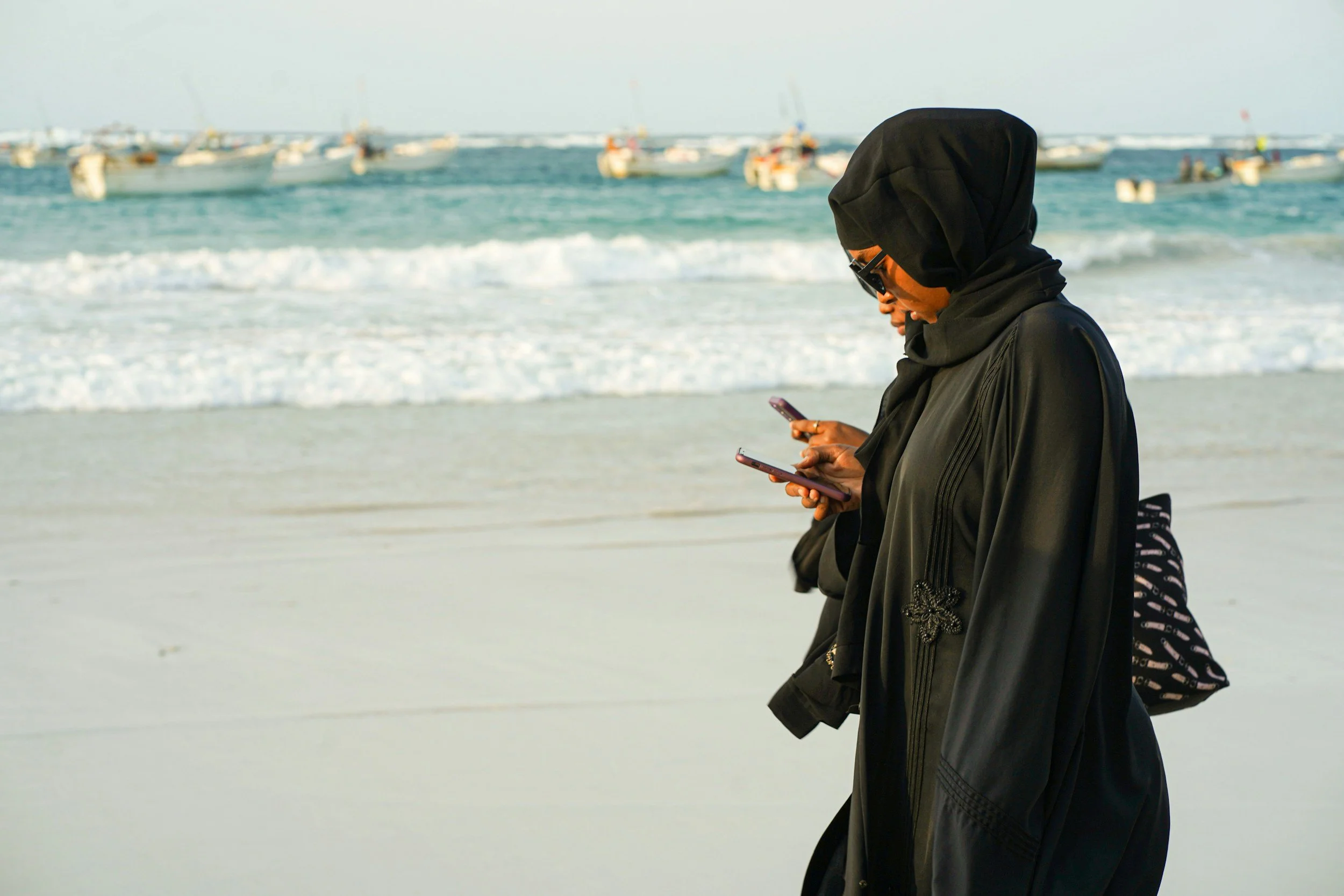 Muslimah texting while walking on the beach.
