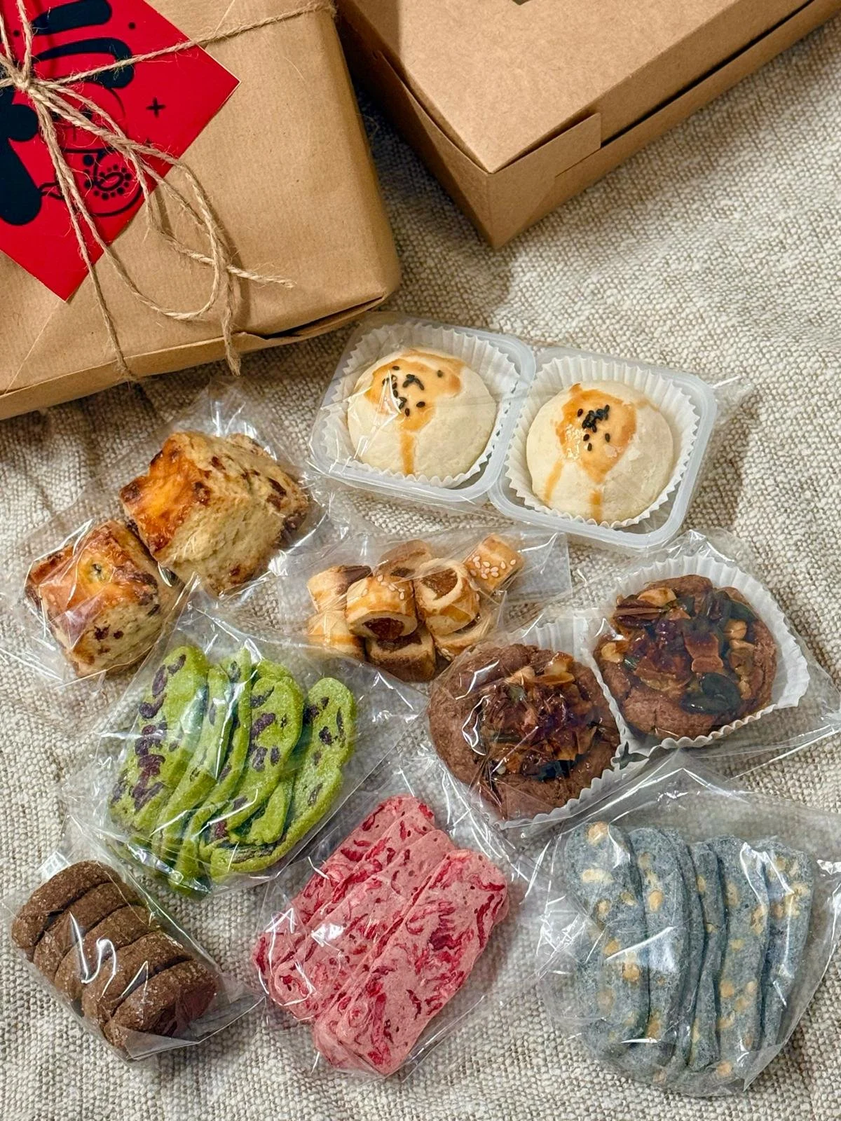 Assorted cookies and baked goods in plastic wrapping with a couple of gift boxes above them.