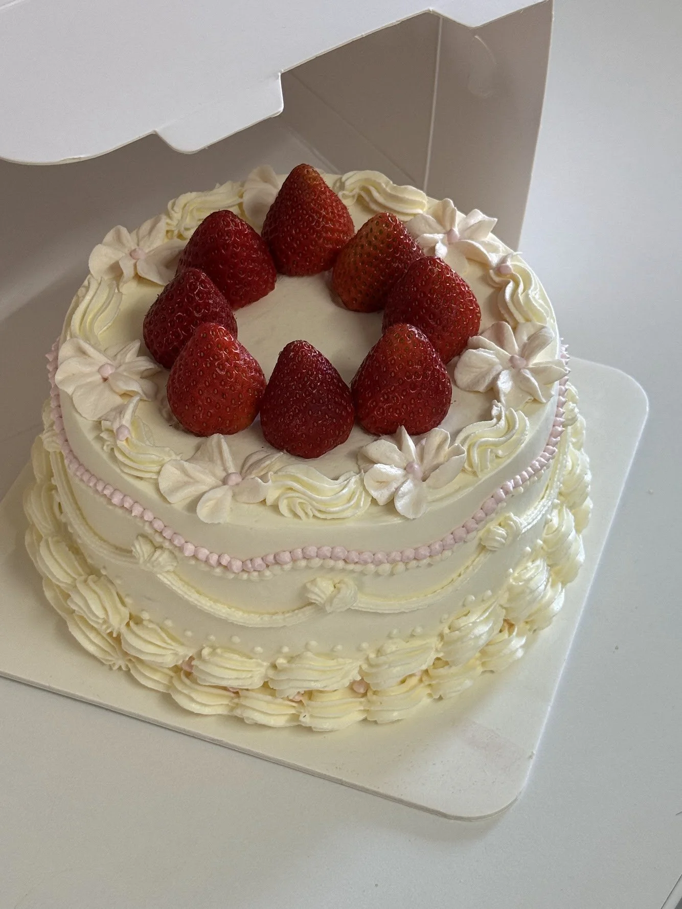 A round white cake decorated with strawberries and pink and white icing flowers on top.