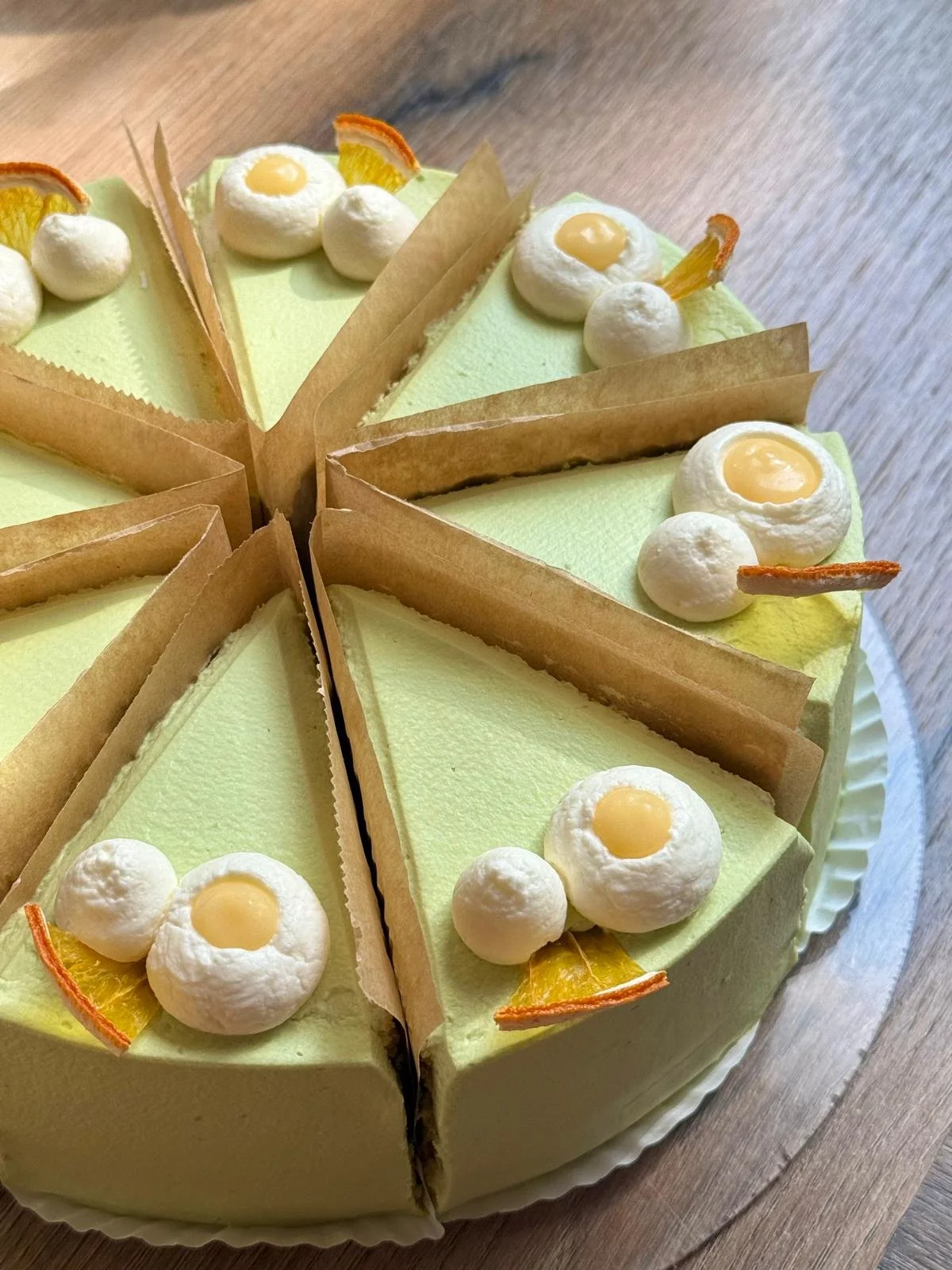 A sliced lemon cake with pale green frosting, decorated with whipped cream, lemon slices, and lemon curd filling on top.