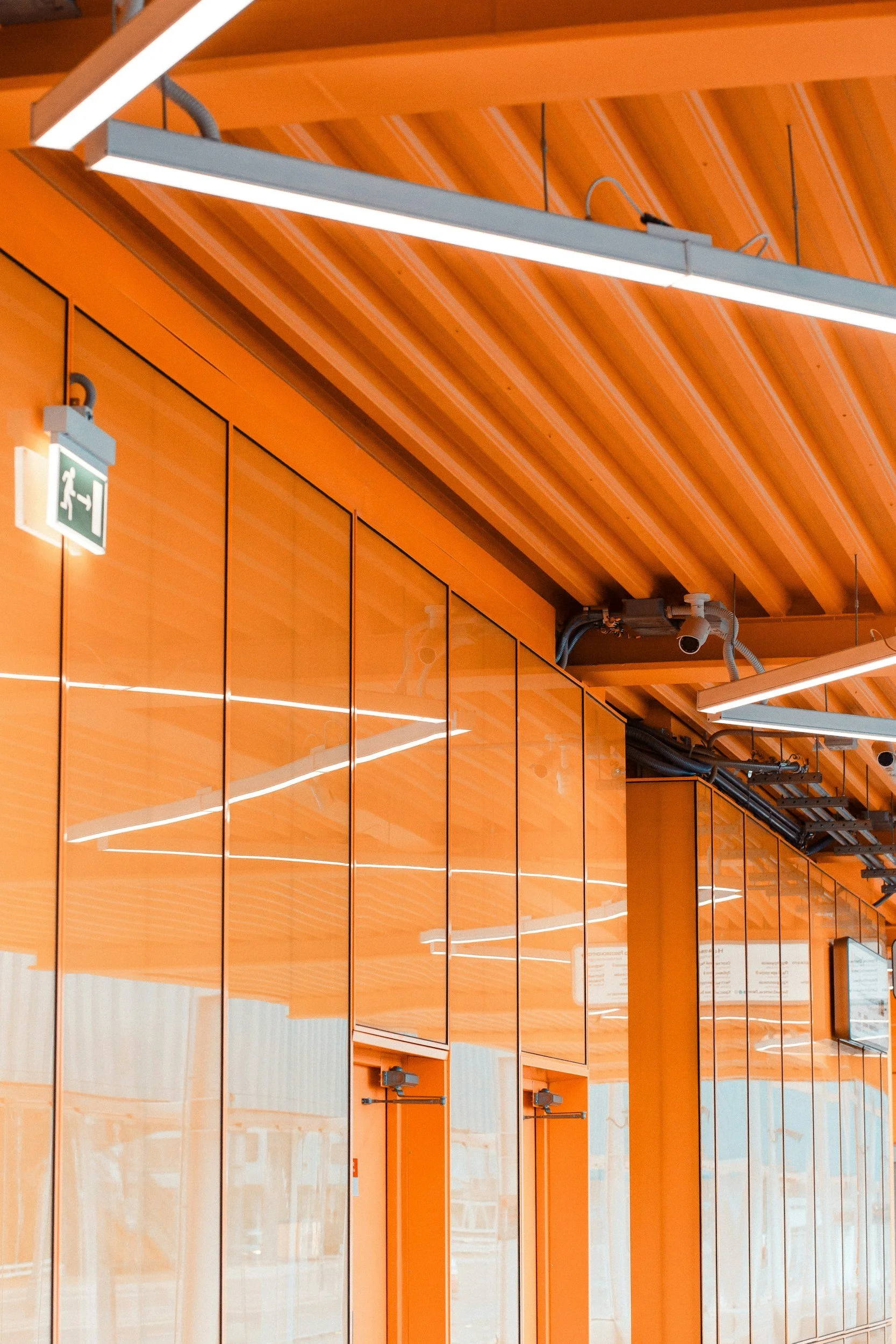 Orange interior space featuring reflective panels, ceiling lights, and a green exit sign.