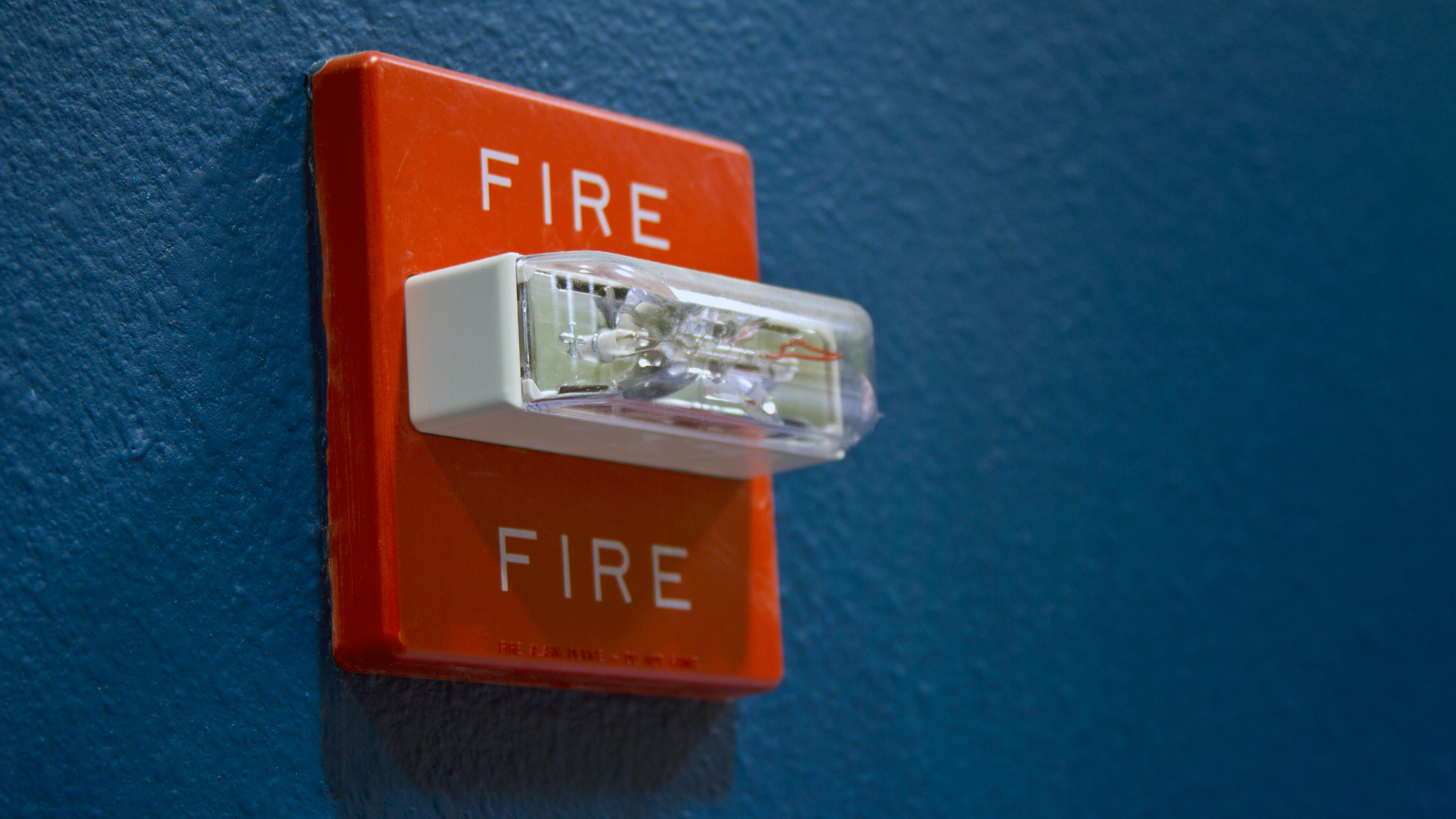 A red fire alarm pull station on a dark blue wall.