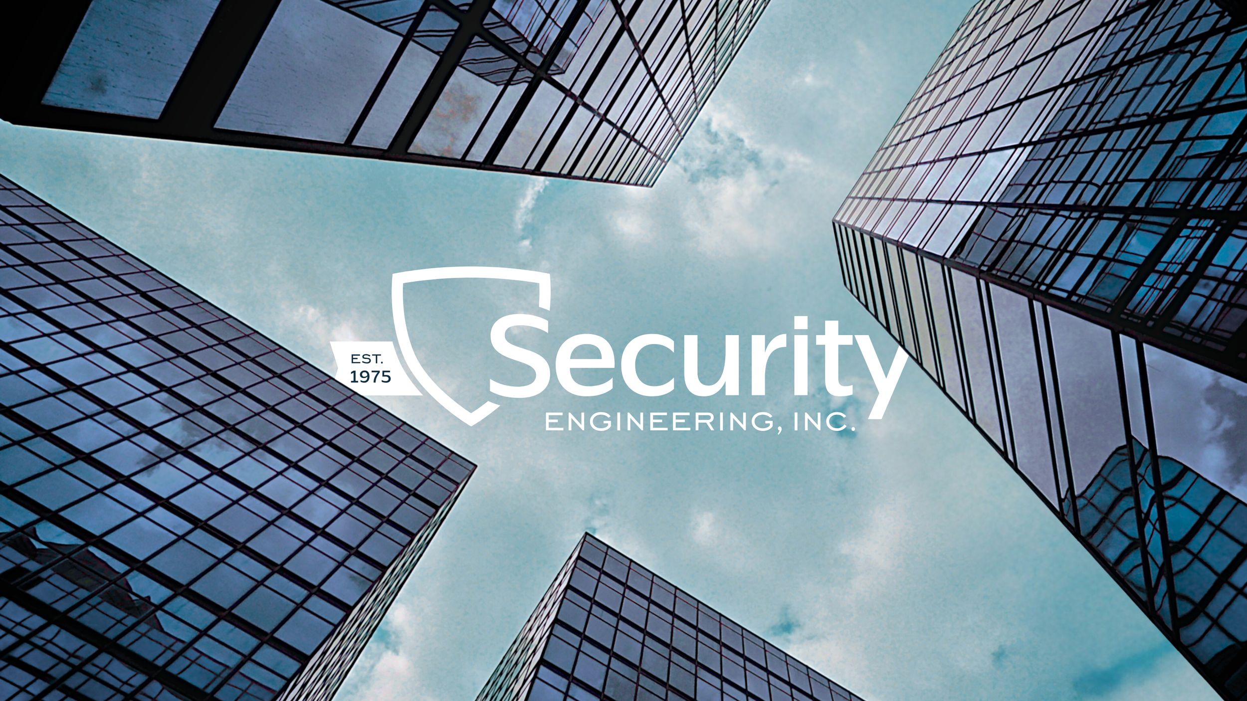 View of tall modern glass office buildings from below against a cloudy sky, with a overlay of the Security Engineering, Inc. logo.
