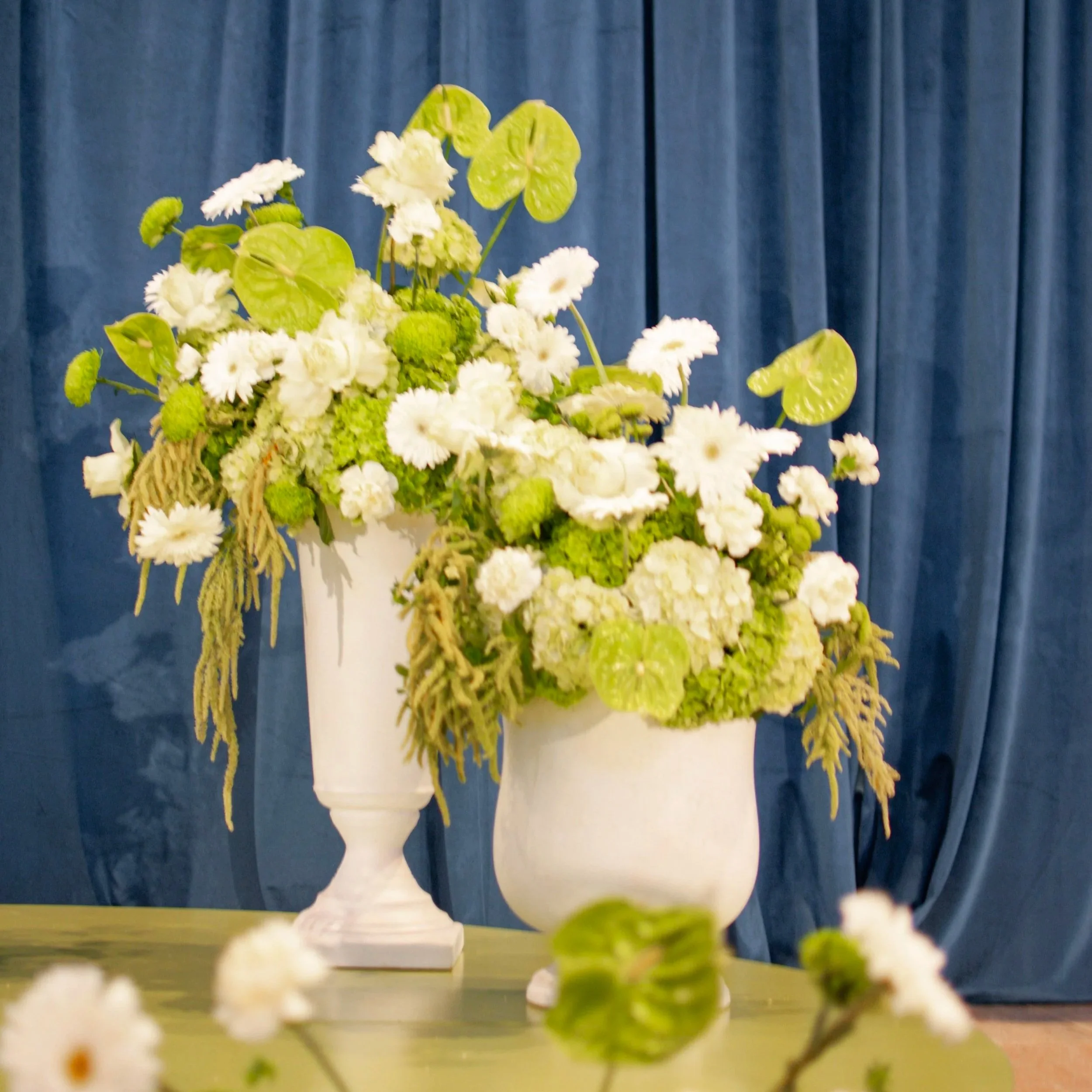 Event installation with two large white urns featuring flowers in shades of lime green and white. Designed by St. Louis Florist, Suncrest Blooms.