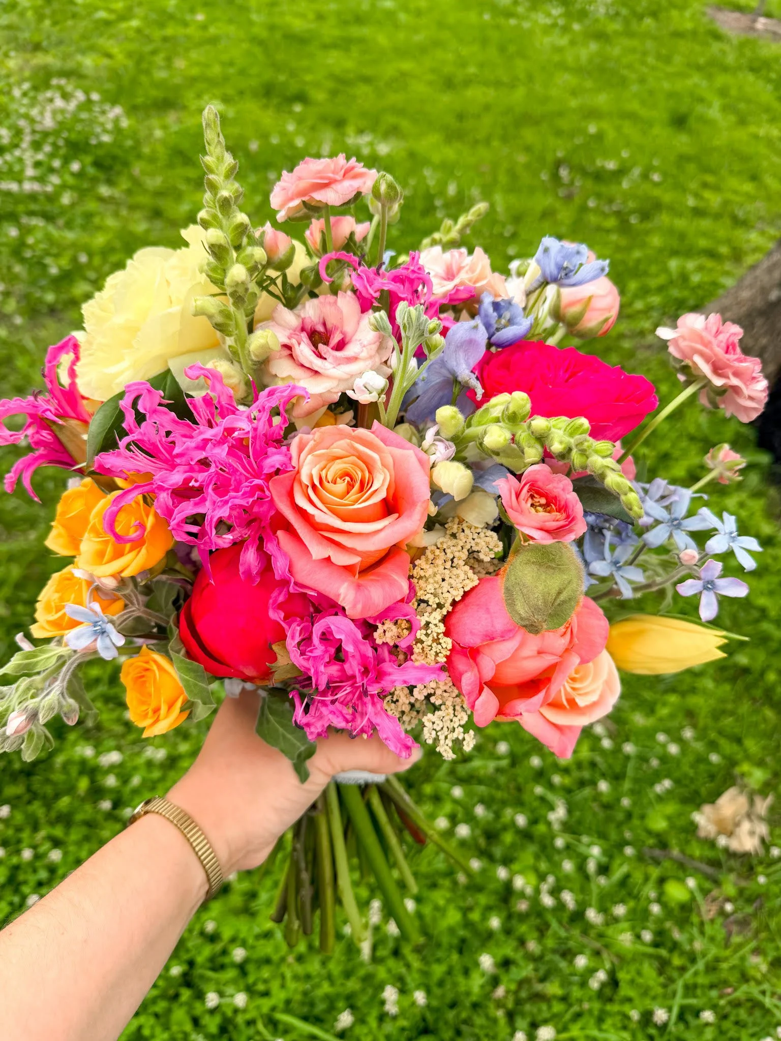Colorful bridal bouquet held in front of grass. Designed by St. Louis Florist, Suncrest Blooms.