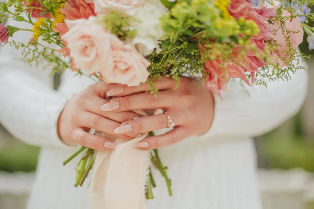 Person in white dress holding a bouquet of pink, white, and green flowers, with a diamond engagement ring on their left hand. Designed by St. Louis event florist, Suncrest Blooms.