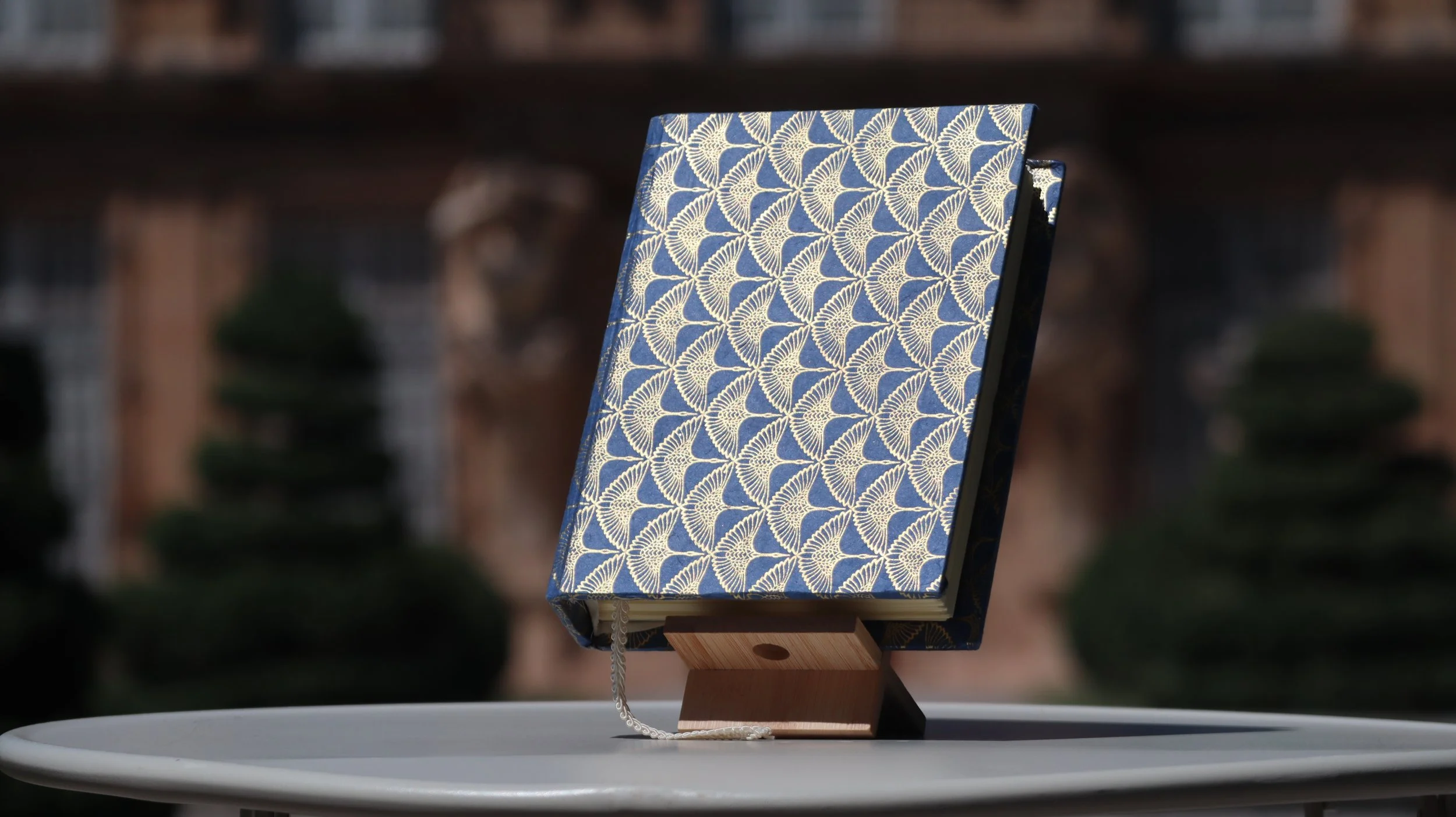 Livre avec couverture bleue et motif doré, posé sur un support en bois, placé sur une table