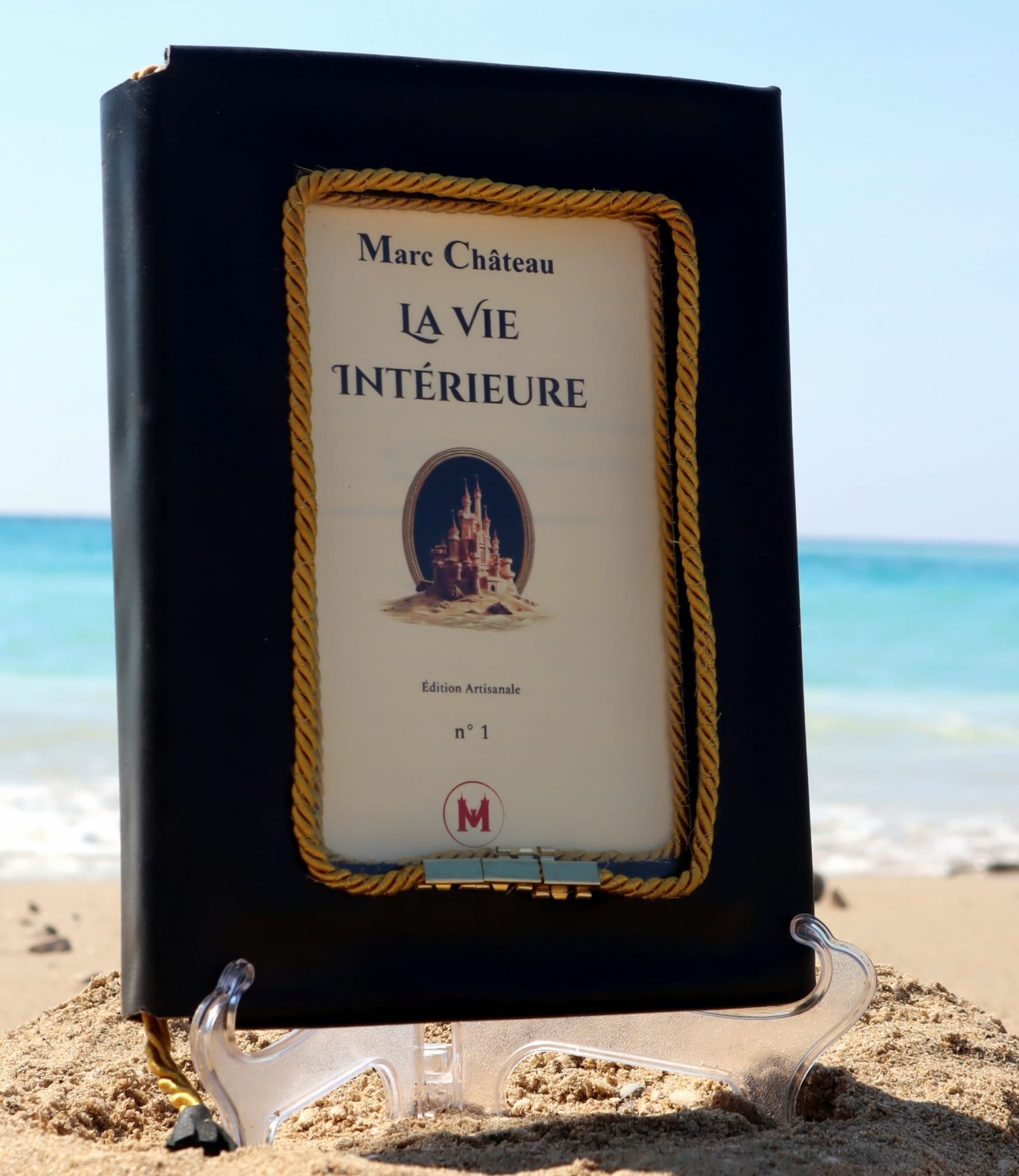 Livre intitulé 'La Vie Intérieure' de Marc Château, édition artisanale, placé sur le sable d'une plage avec la mer en arrière-plan.
