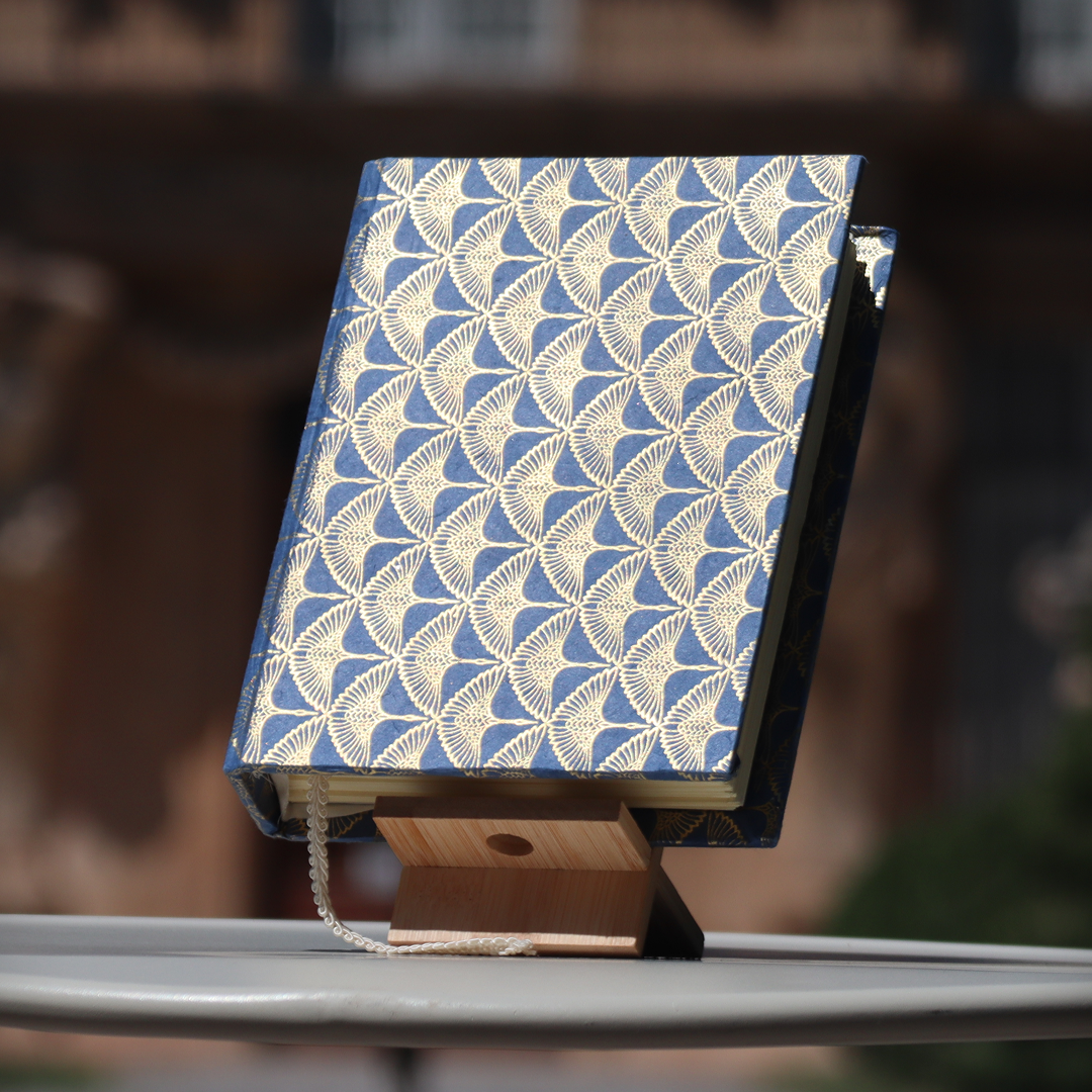 Un livre avec une couverture bleue à motif de feuilles dorées, posé sur un socle en bois, avec un cordon blanc suspendu à la couverture.
