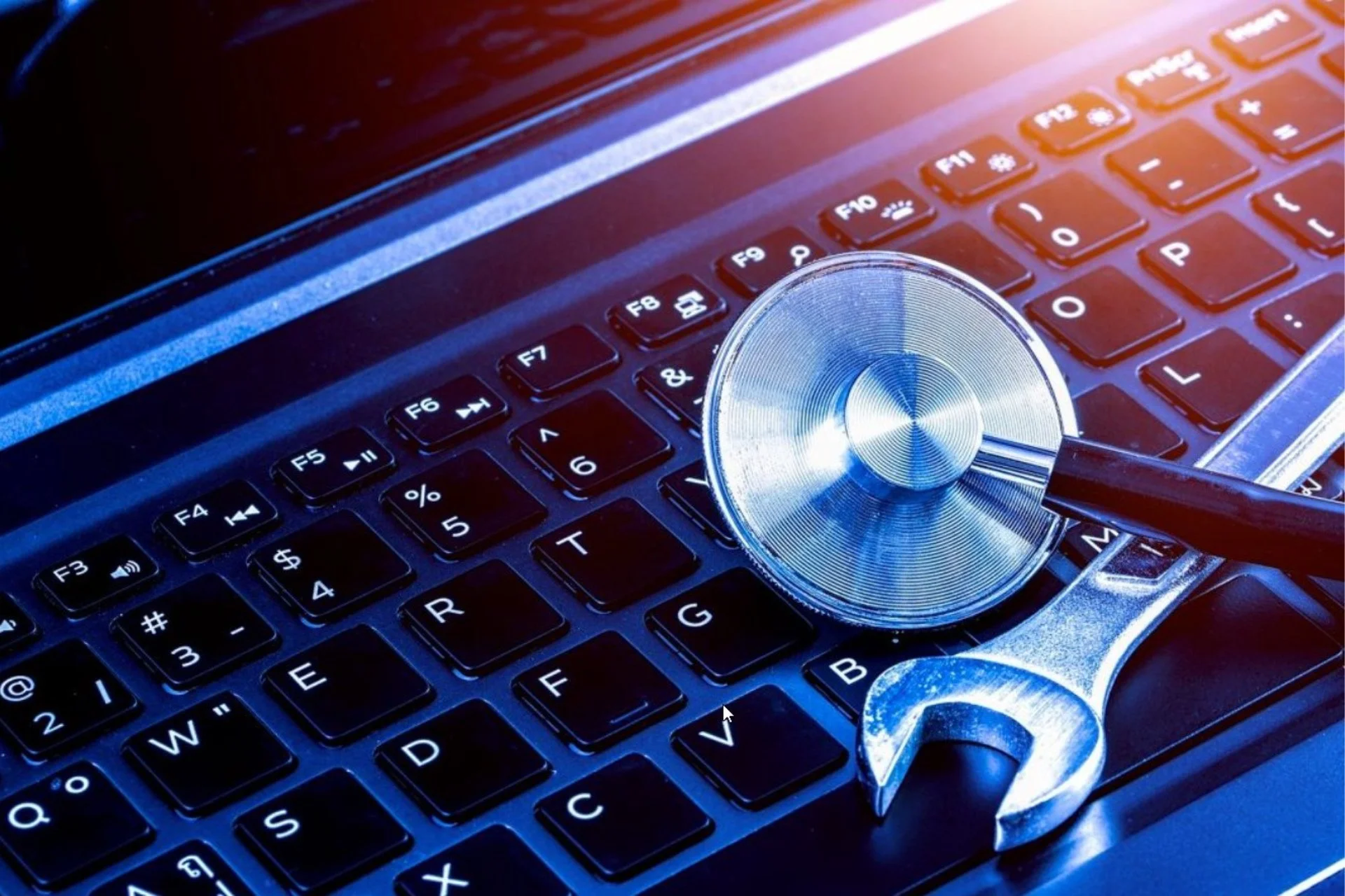 Close-up of a computer keyboard with a stethoscope and wrench resting on it, illustrating technical support or medical technology.