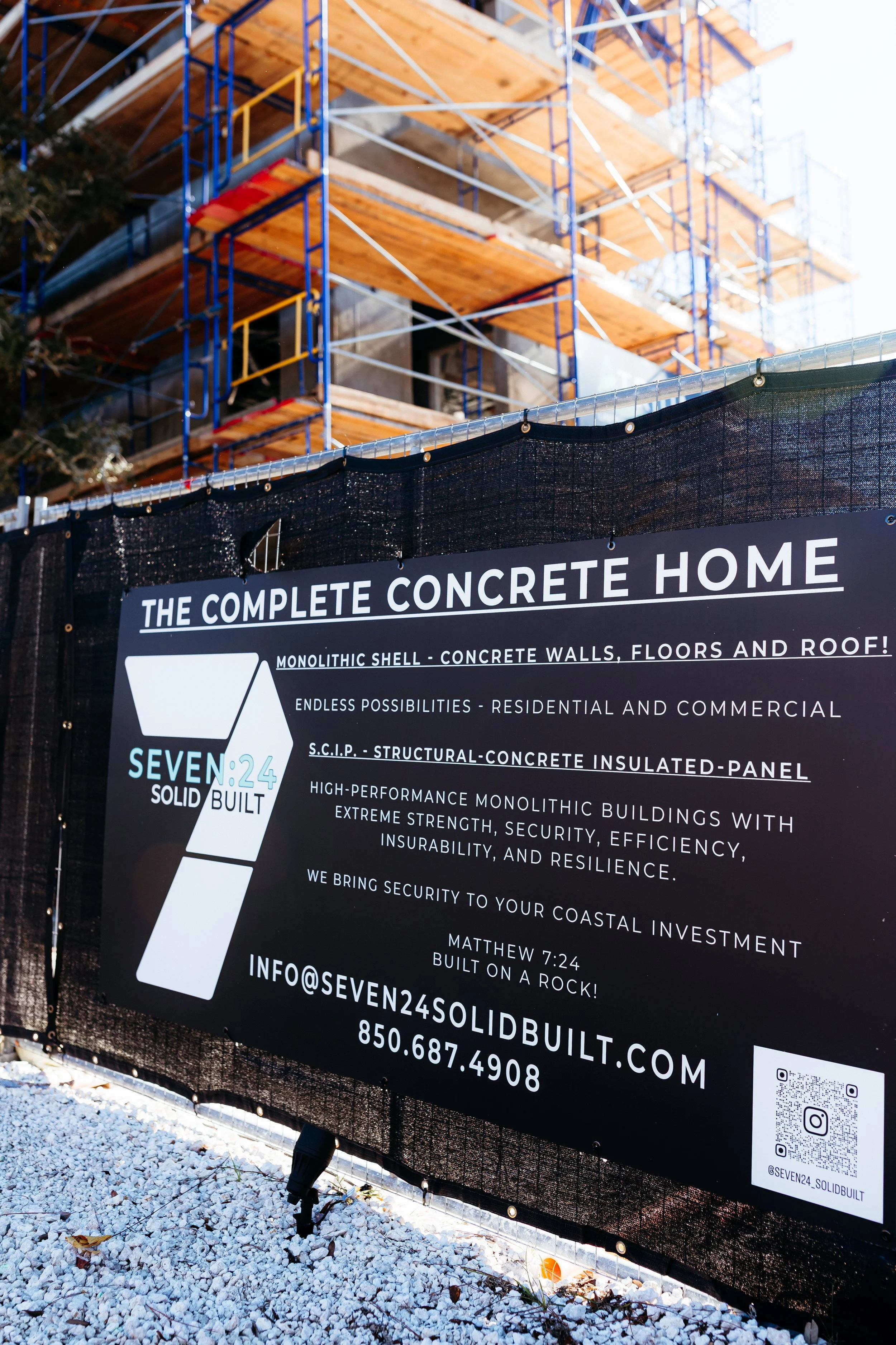Construction site with the framework of a house under construction and a sign advertising the benefits of concrete homes.