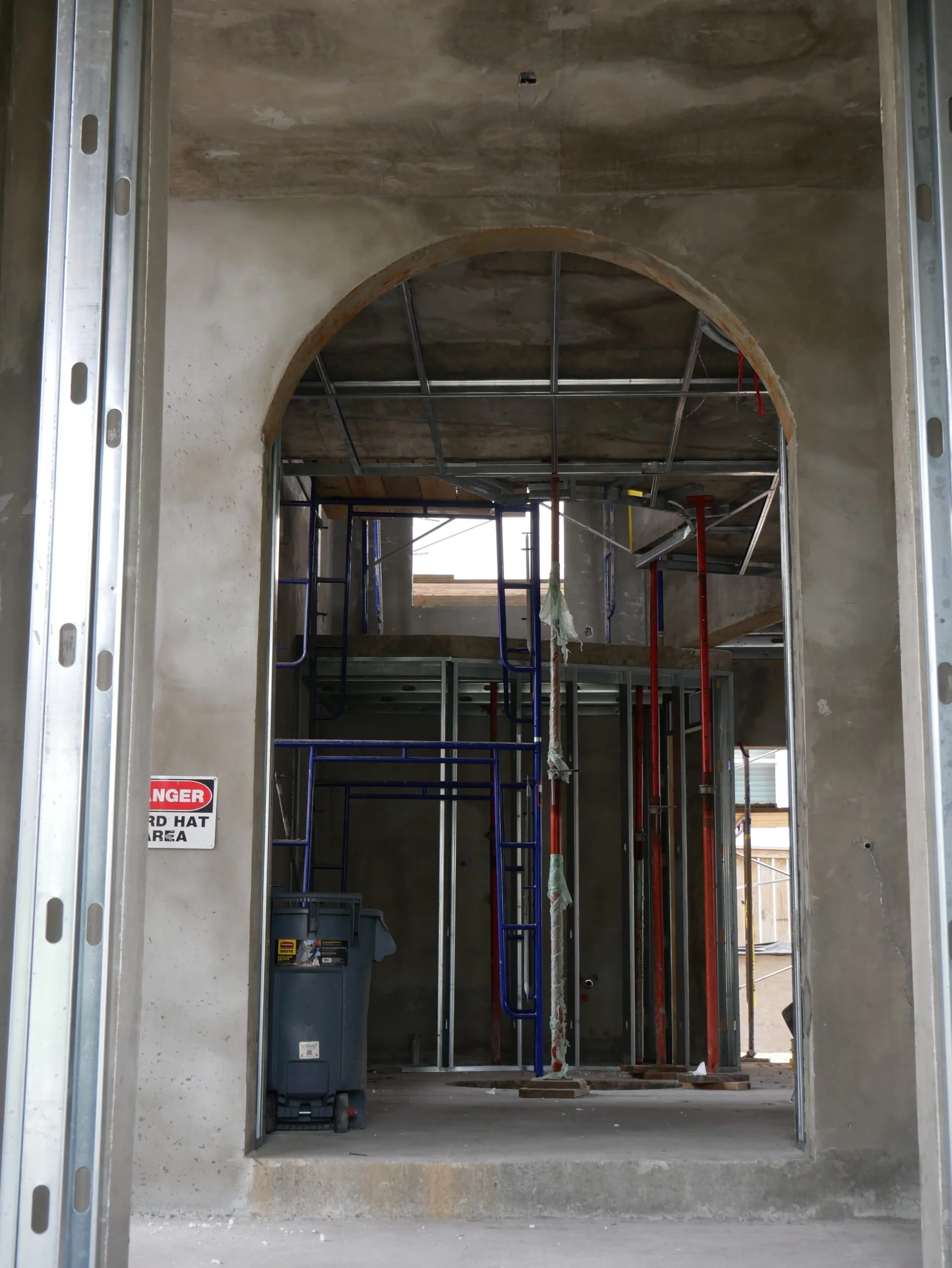 Interior of a building under construction with exposed framing, scaffolding, and a warning sign.