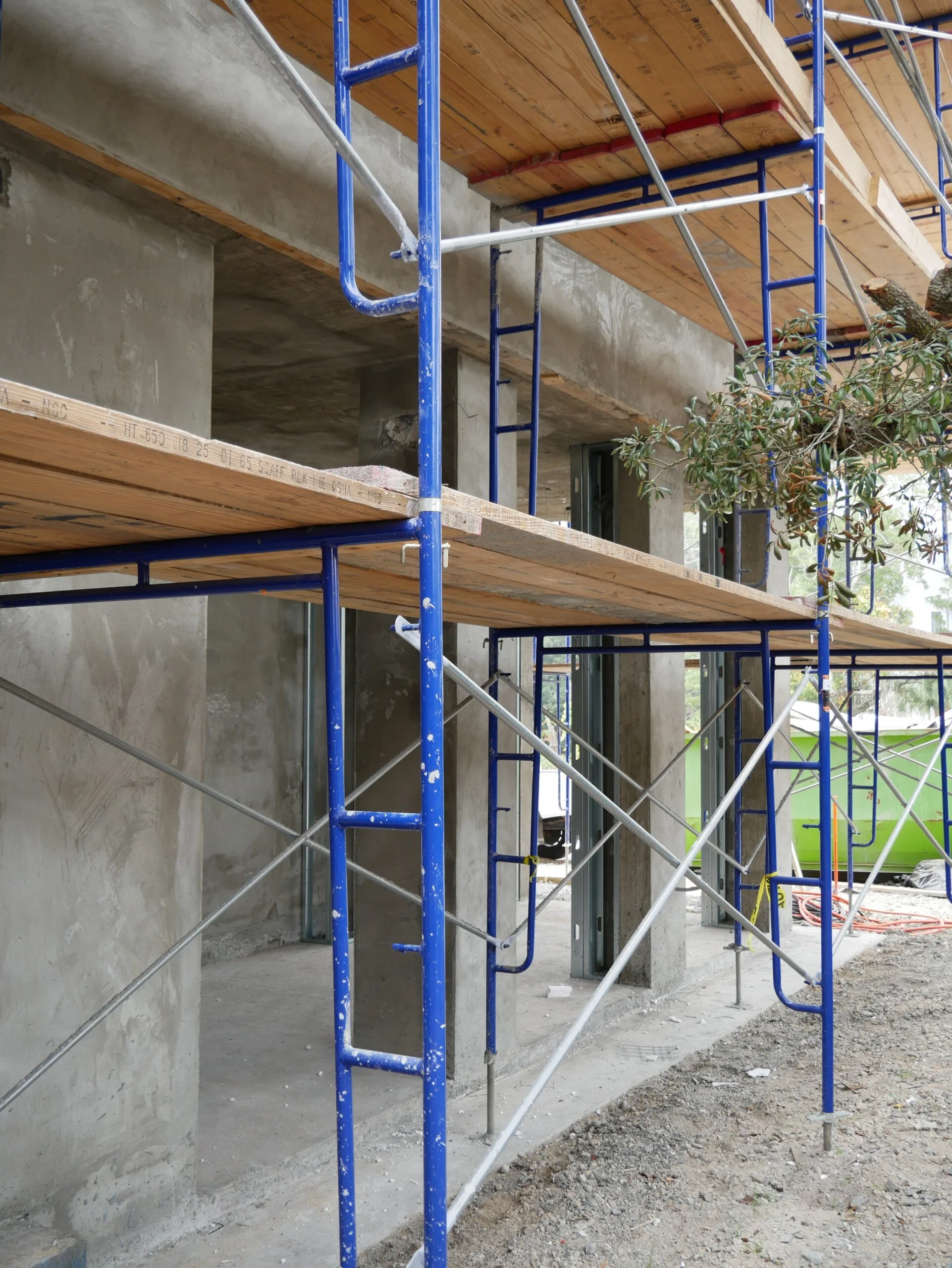 Construction site showing scaffolding with wooden planks, concrete walls, and a partially built structure.