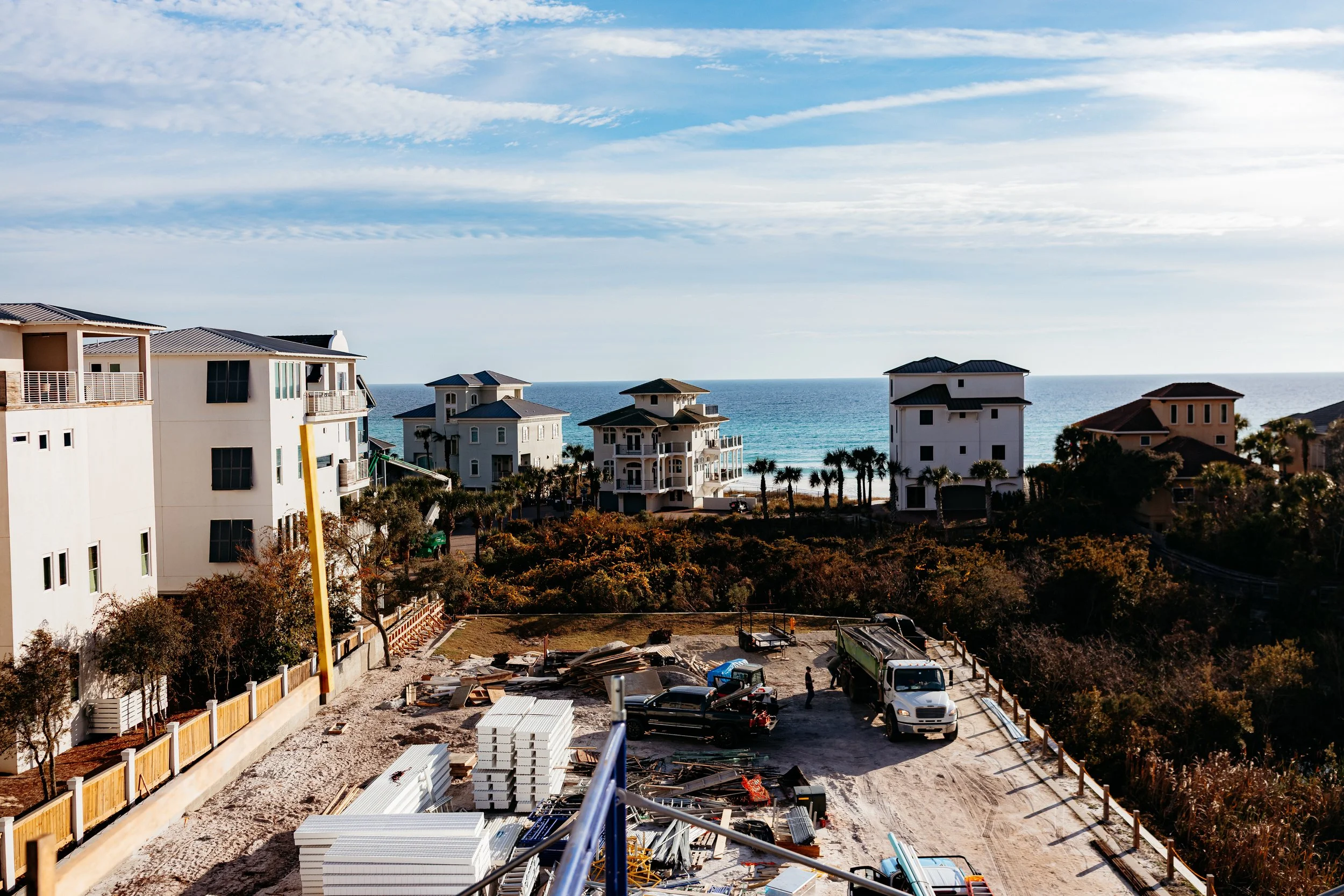 View of beachfront houses under construction, with construction materials and vehicles, overlooking the ocean and sky.