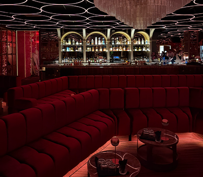 Luxurious bar with red curved sofa seating, illuminated shelves with bottles, and modern ceiling design.