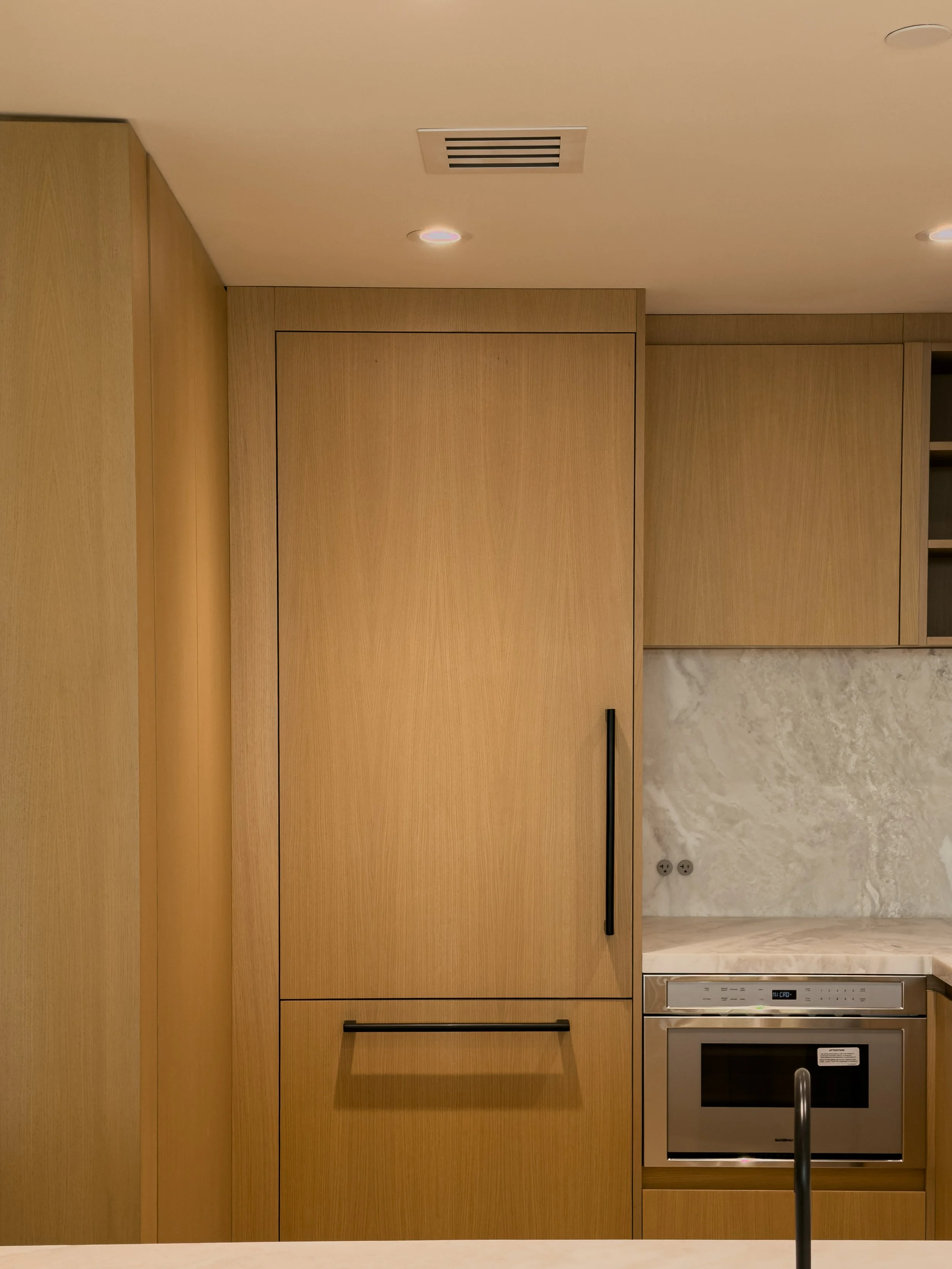 Modern kitchen with wooden cabinets, built-in oven, marble backsplash, and ceiling vents.