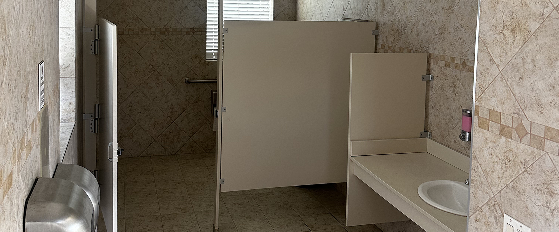 A pathway leading to tennis courts with about four rectangular plant beds and a small white stool on the concrete surface.