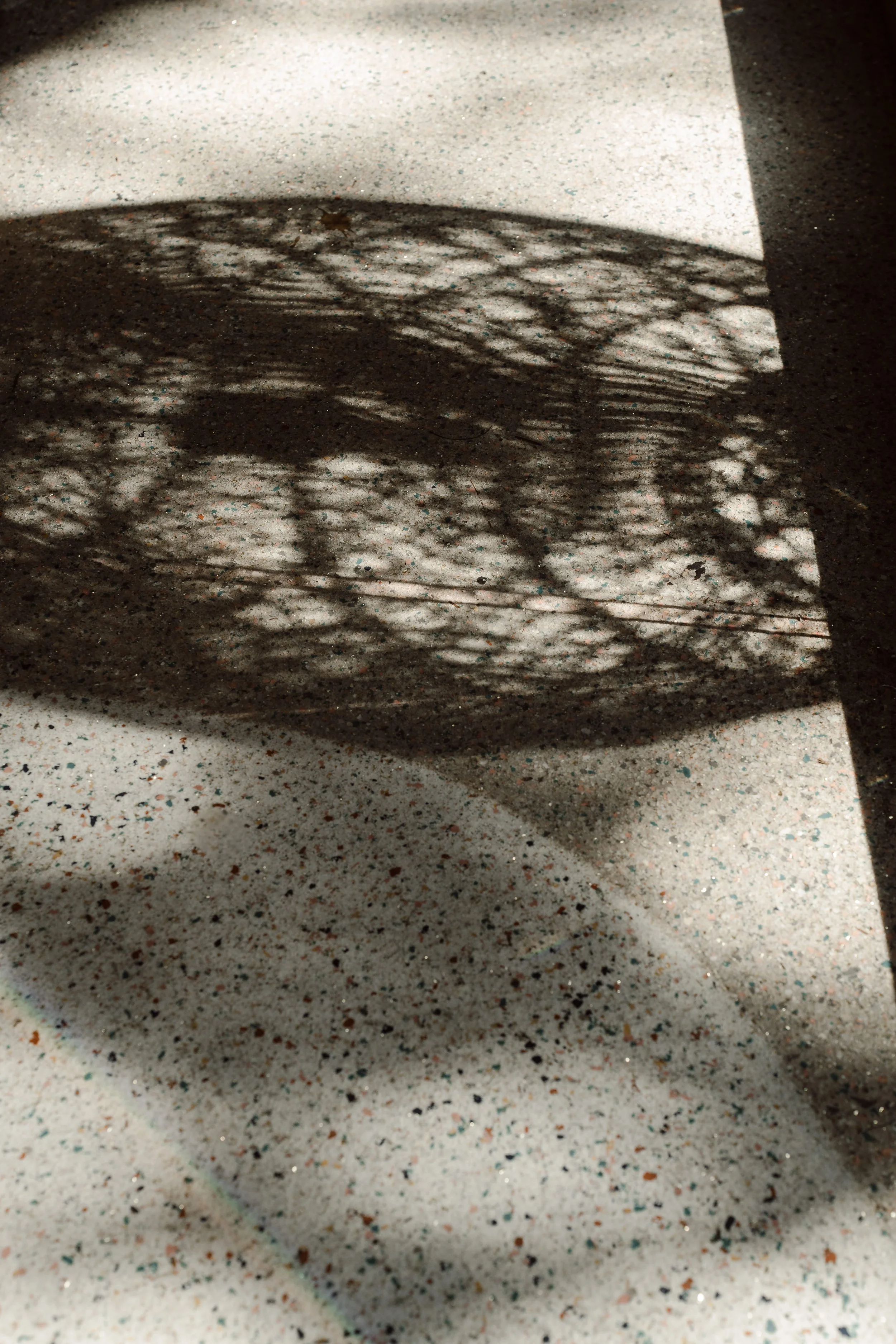 Shadow of a wire basket cast on a speckled countertop with a nearby wall.