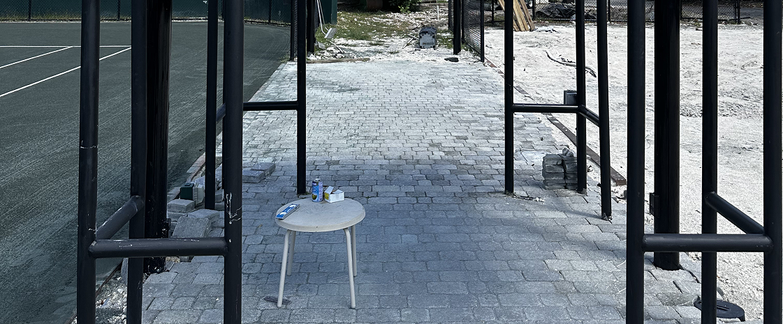 A paved walkway under construction with black metal frames erected along the sides, and a small white table with cans and a phone on it.
