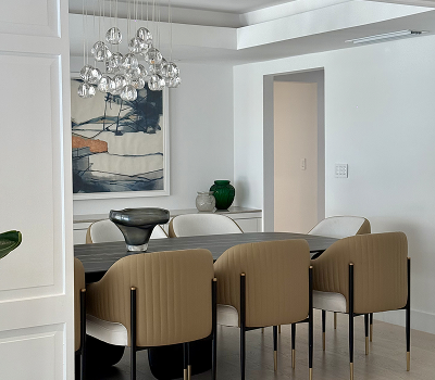 Modern dining room with beige chairs around a dark wooden table, abstract wall art, chandelier, and decorative vases.