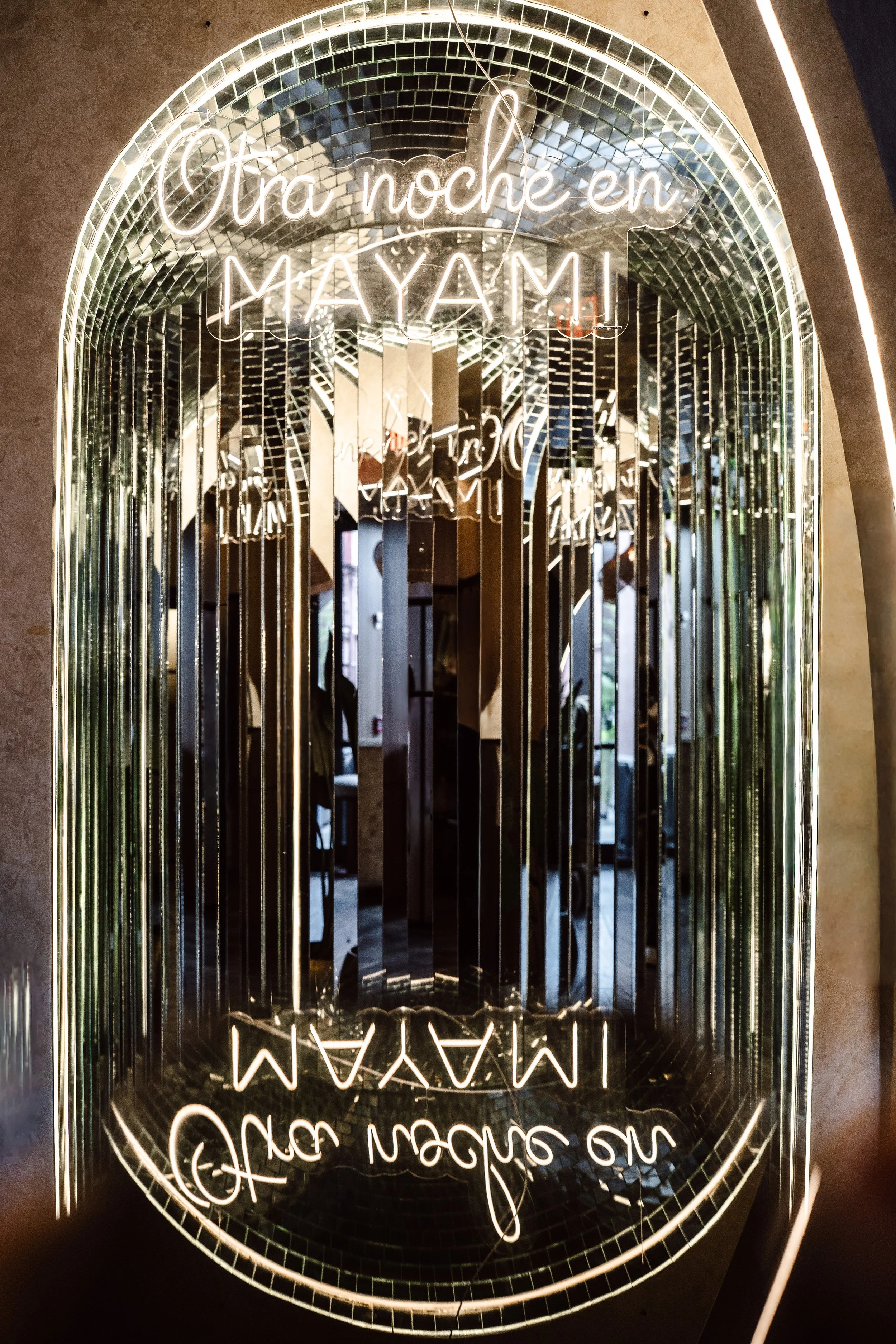 Neon sign with Dutch phrase 'Ora noche en MAYA' and decorative mirrors behind it.