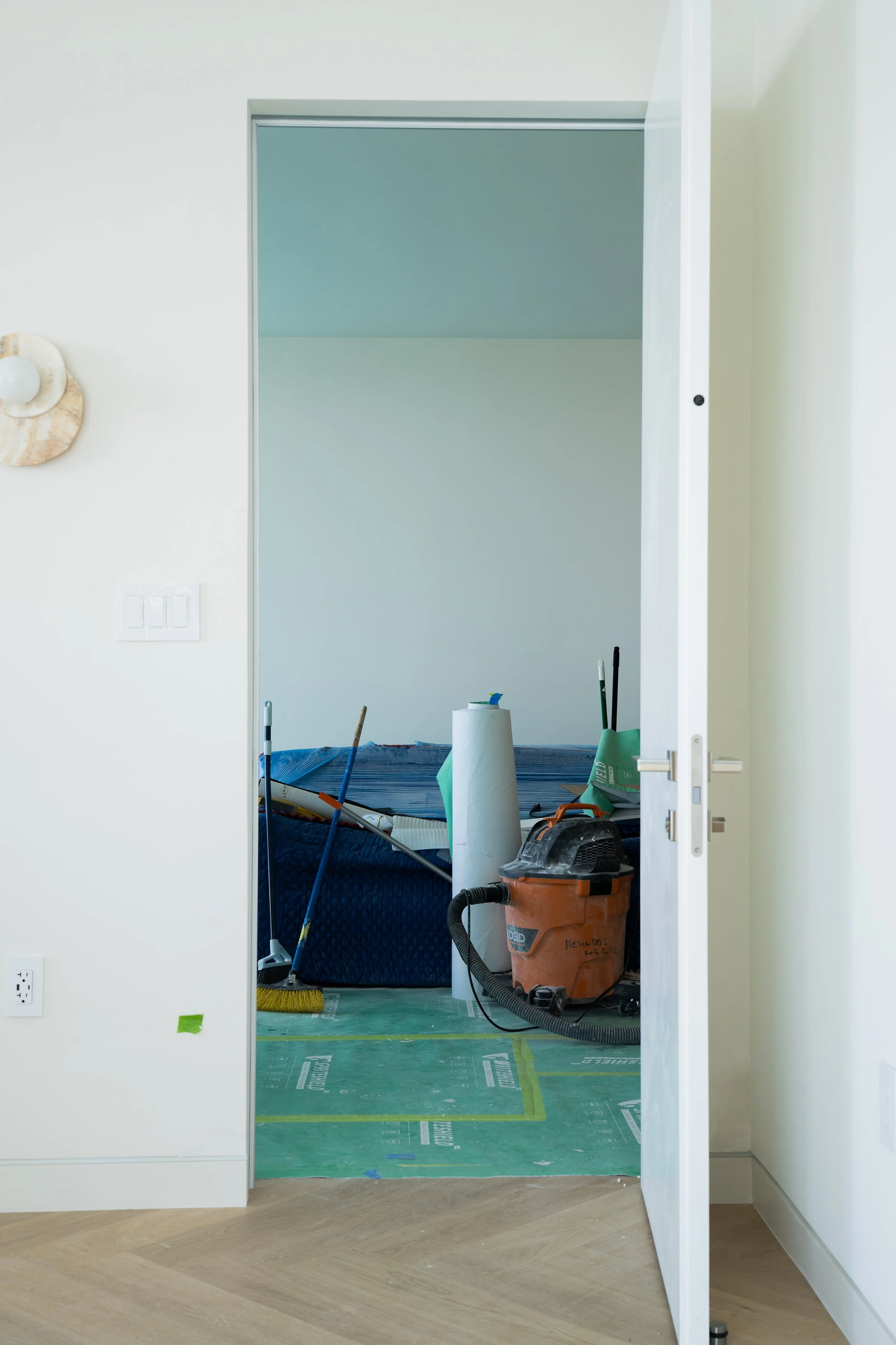 Interior of a room under renovation, viewed through an open door, with construction tools and supplies inside.