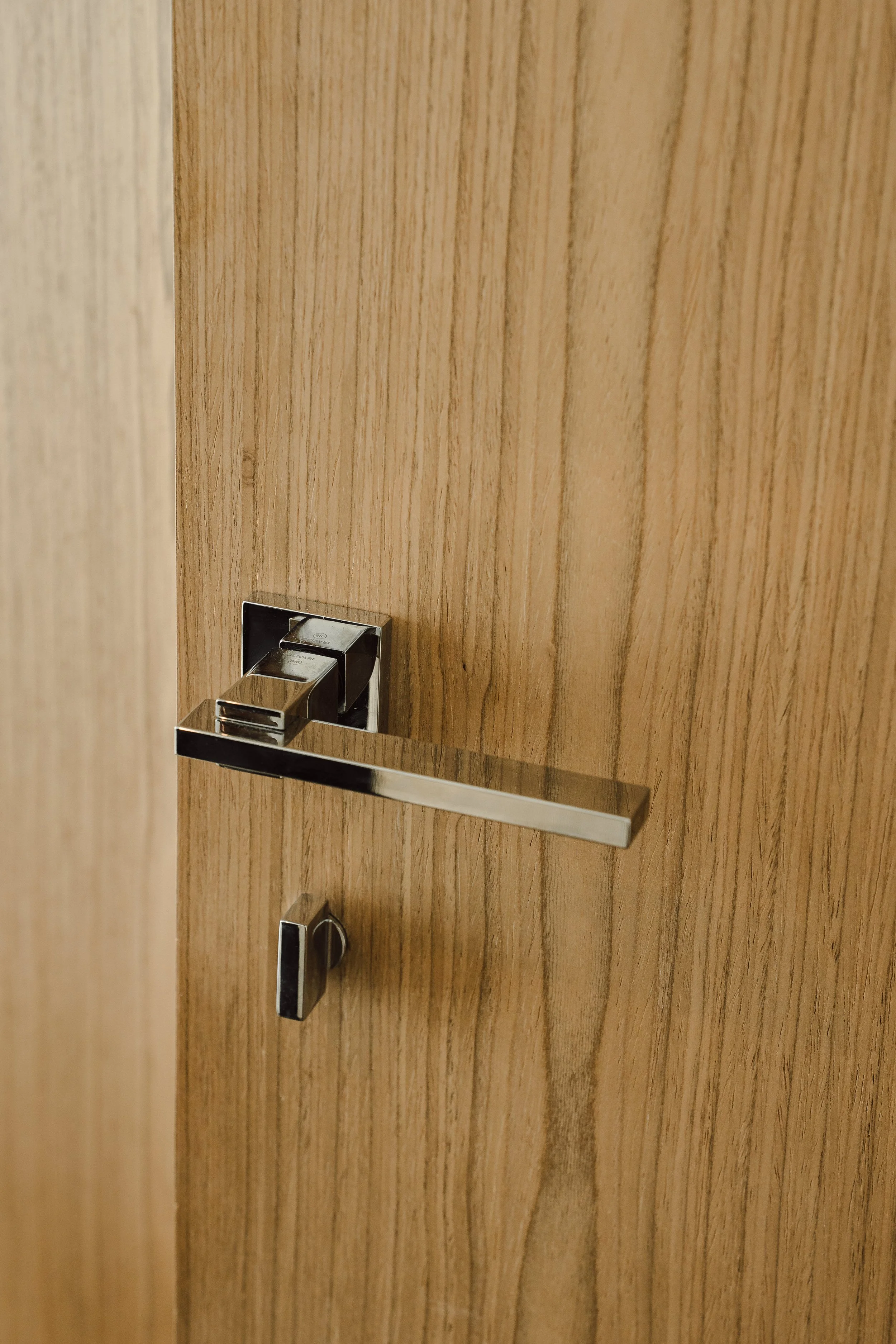 Close-up of a modern silver door handle with a rectangular base mounted on a wooden door with a vertical grain pattern.