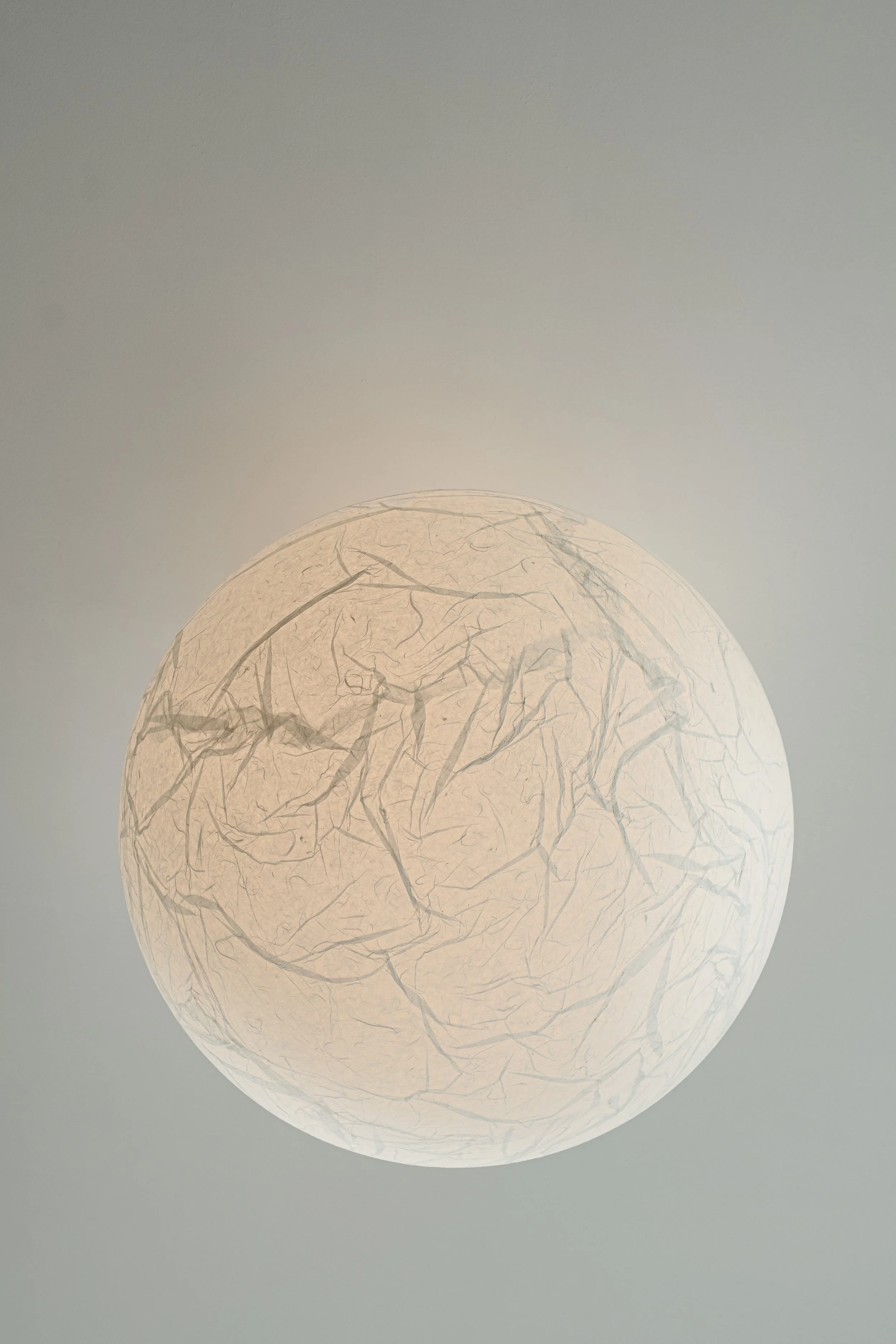 A round paper lantern with a crinkled pattern, glowing softly against a plain background.