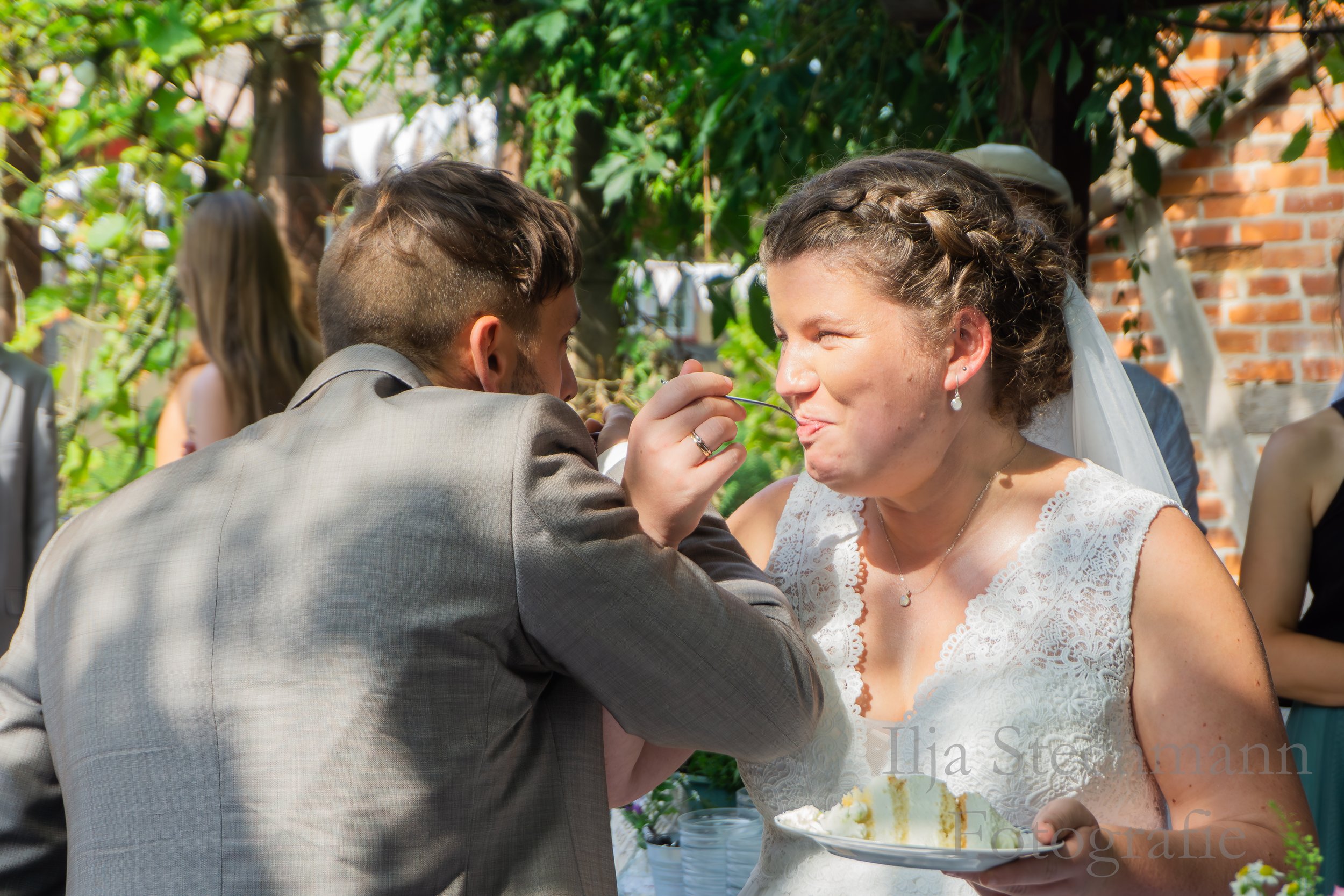 Ein Brautpaar bei einer Hochzeit in Lübeck isst gemeinsam ein Stück Kuchen im Garten.
