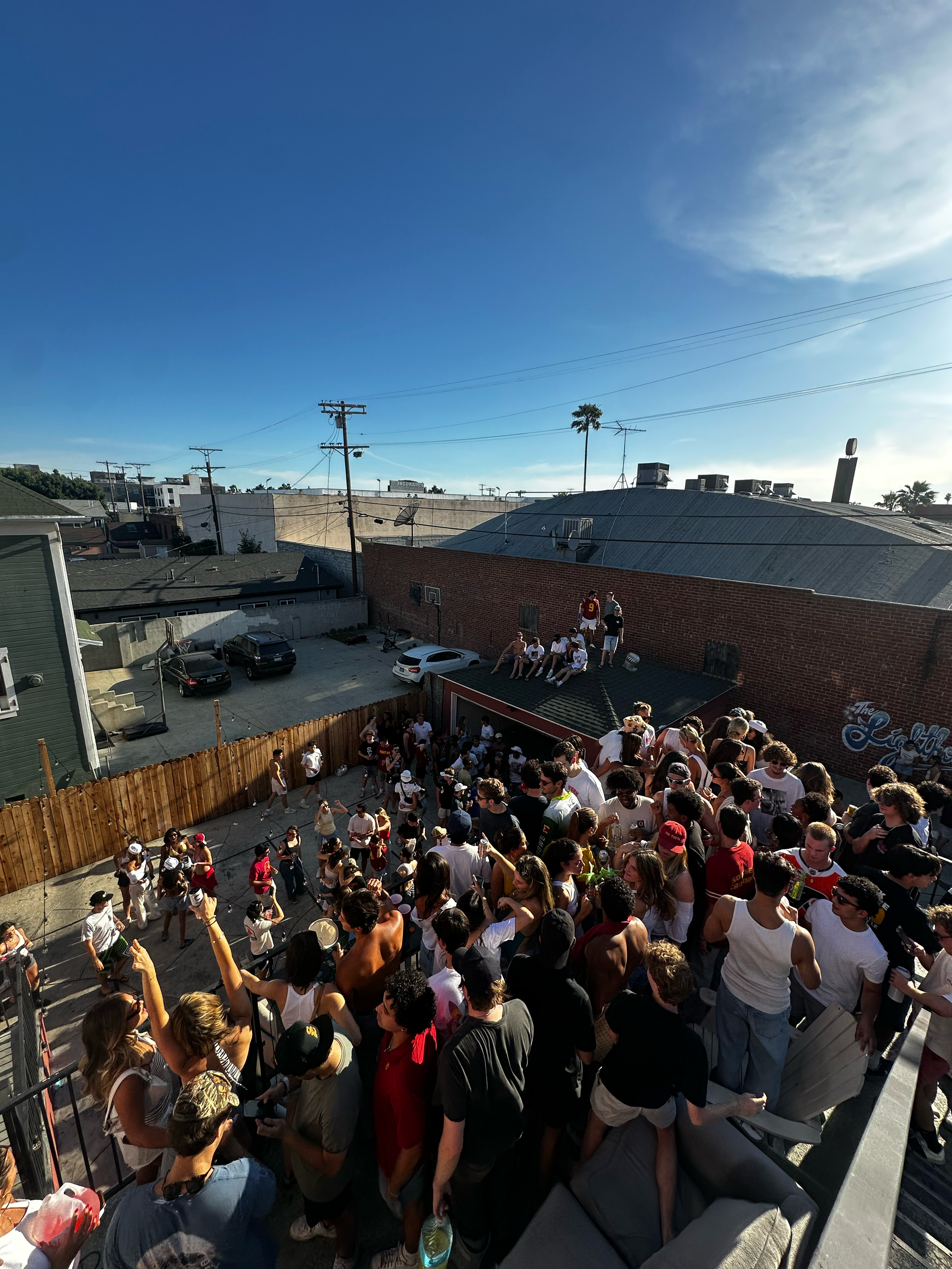 A large crowd of people waiting in line outside a building with a sign that says 'The Elysian.' The line extends along the sidewalk, and the sky is clear with some clouds.