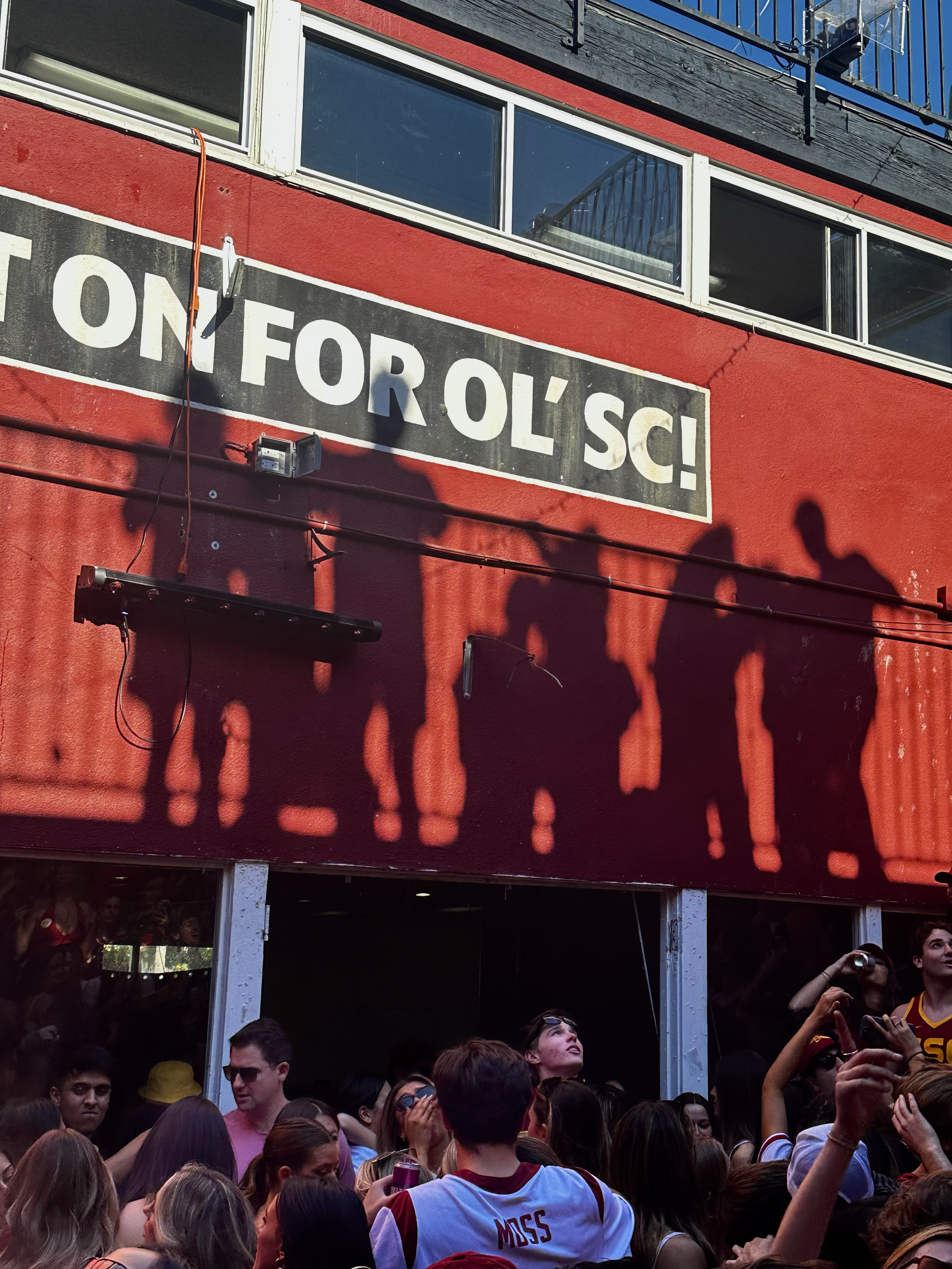 Shadow puppets of people holding hands cast onto a red wall above a crowd at a sports or concert event.