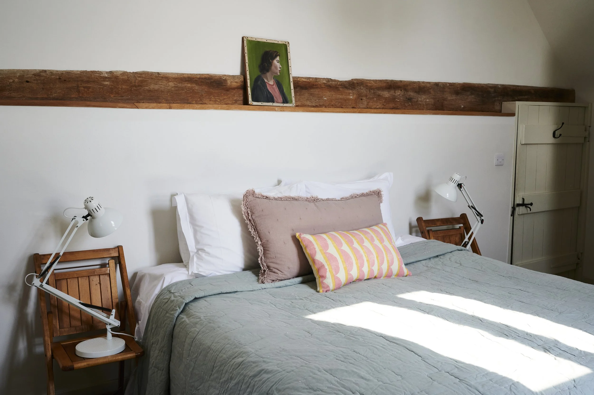 A cozy bedroom with a bed that has white sheets in east sussex providing farm cottages for big groups and weddings with a rustic wooden beam across the white wall.