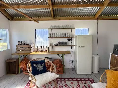 Cozy kitchen corner with a small refrigerator, open shelf with glasses and cups, wicker chairs with pillows, and a patterned rug. Private Campsite Glamping Farm.
