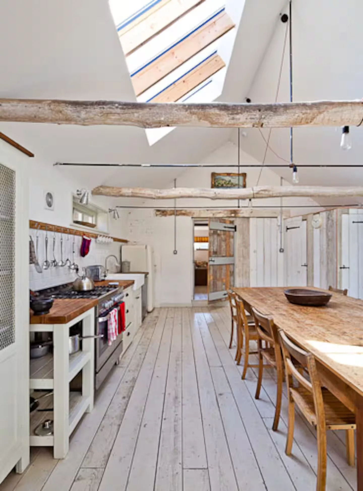 Open farmhouse kitchen and dining area with rustic wood beams and light-colored wooden flooring. A long dining table with chairs is on the right, and a stove, Sussex Group Parties.