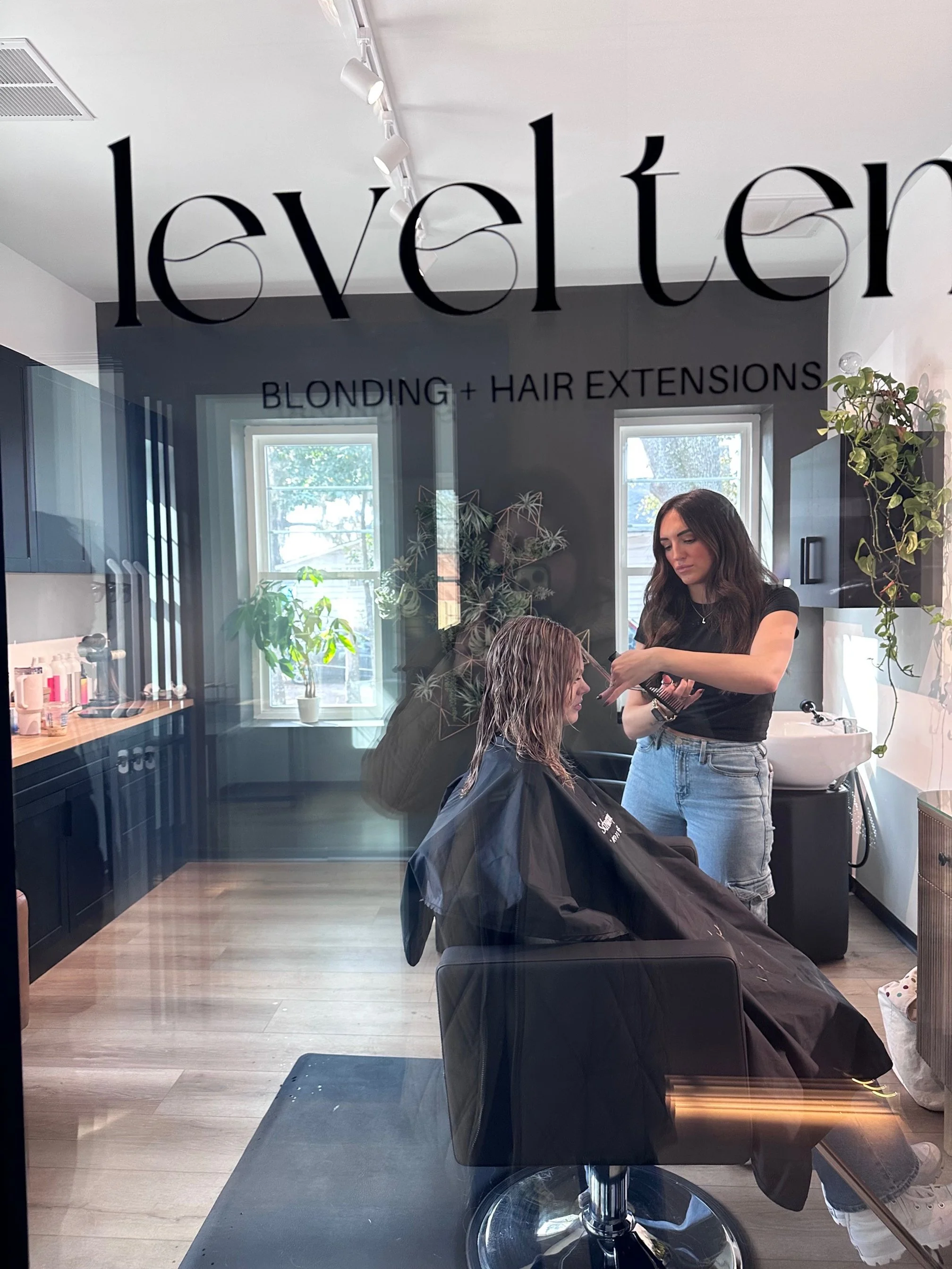 Interior of a hair salon with mirrors, hairdryers, and black chairs. A neon sign on the wall says "You're like really pretty" in white cursive neon lights.