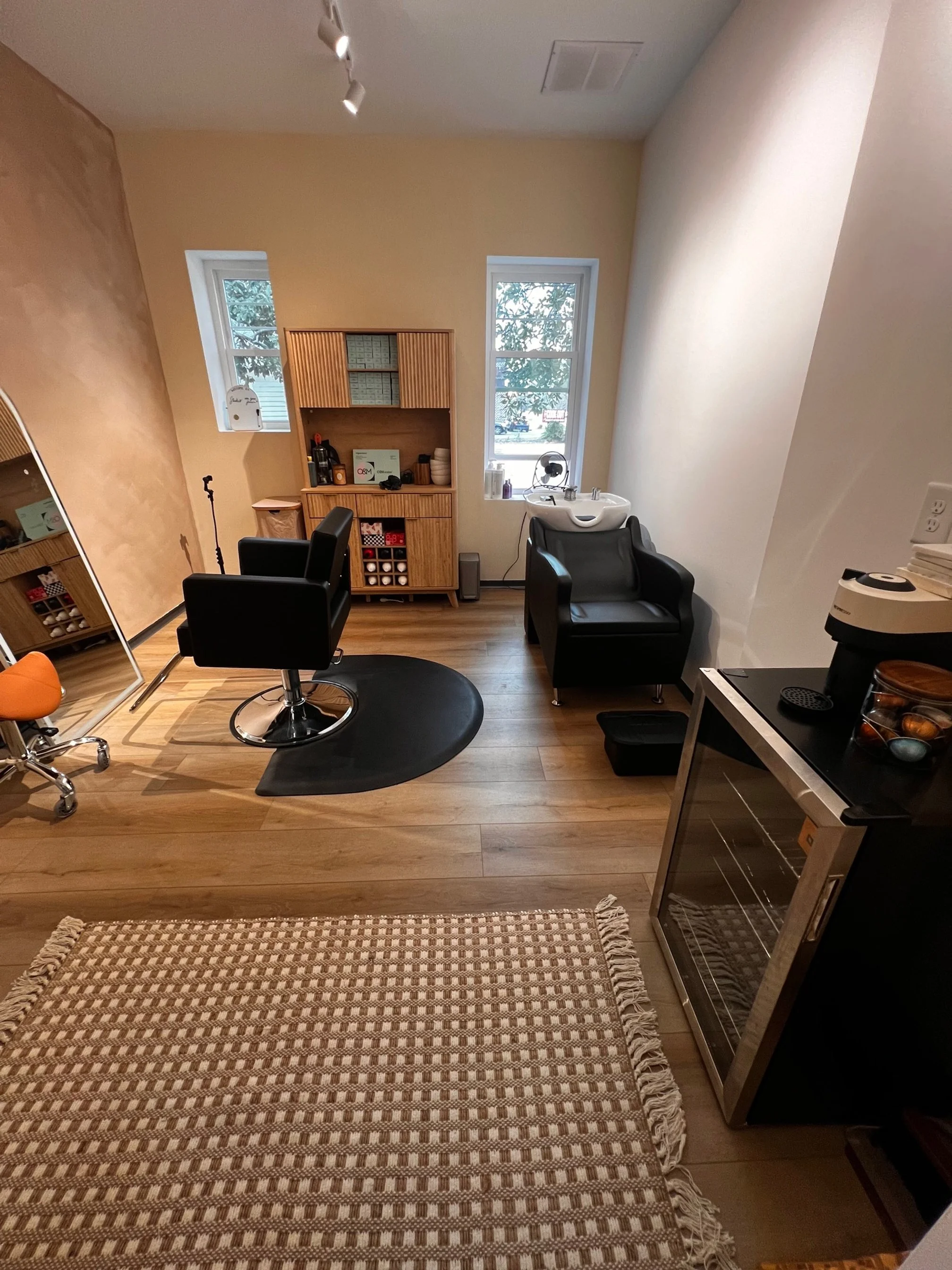 Indoor hair salon with black chairs, oval mirrors, and a white neon sign on the wall that says "You're like really pretty".