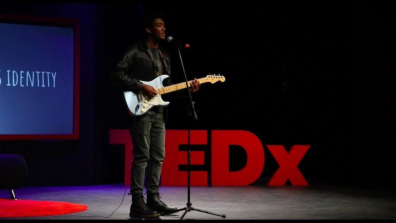 A young person playing an electric guitar on a stage during a TEDx event.