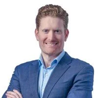 Professional man with short hair and beard, wearing a blue suit and light blue shirt, smiling with arms crossed