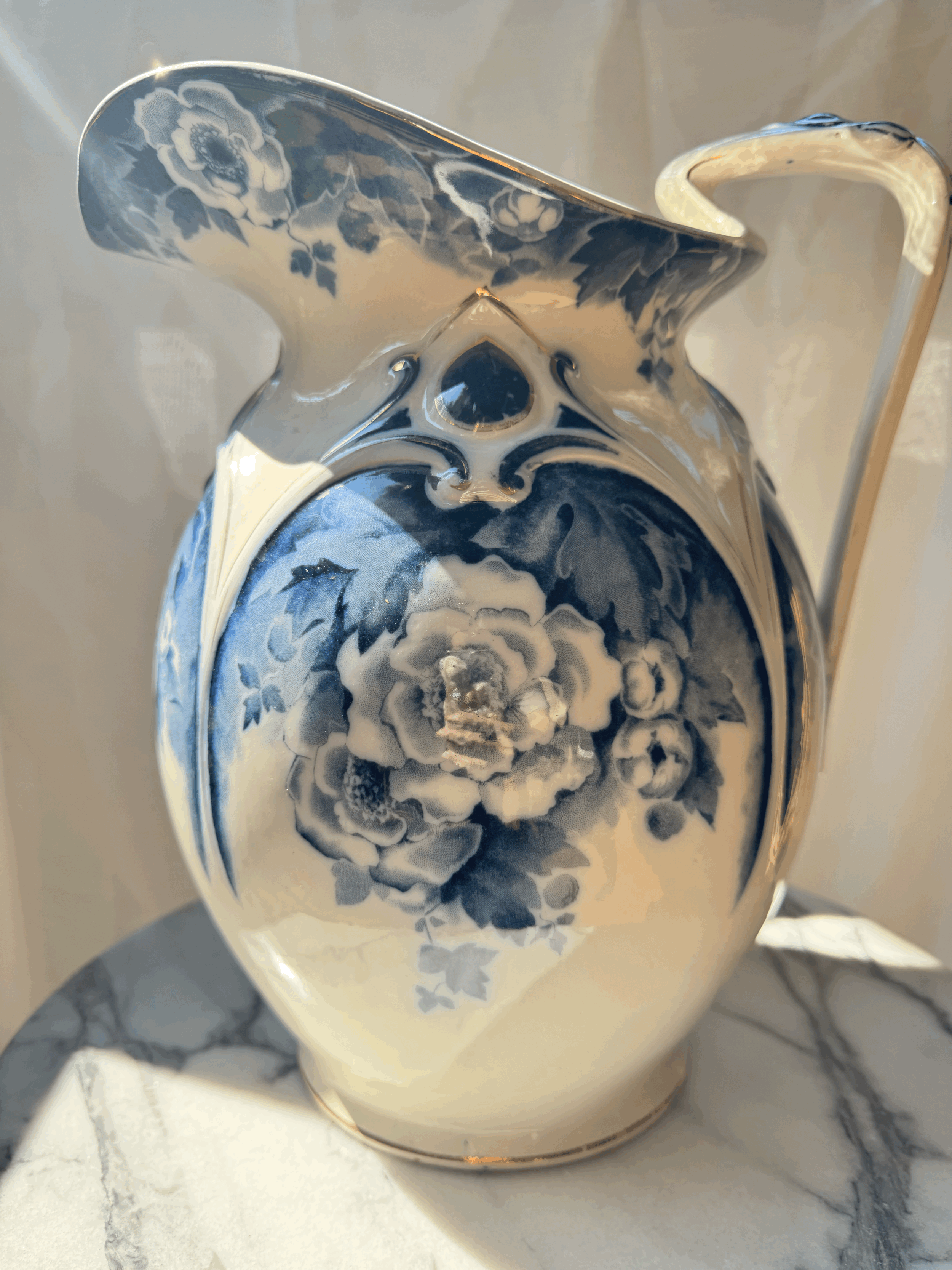 A porcelain pitcher decorated with blue and white floral patterns sitting on a marble surface.