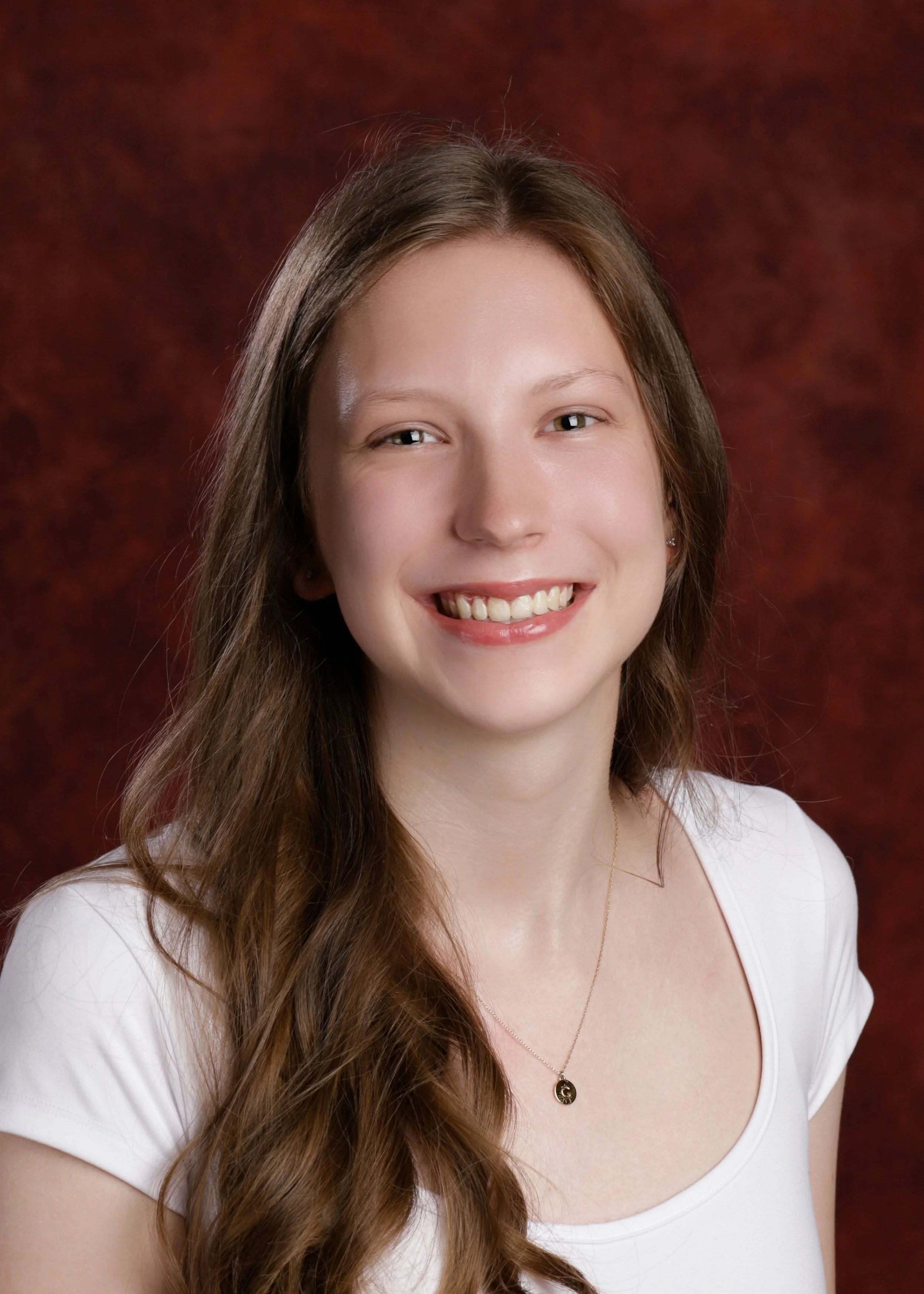 Photograph of Claire Hermitage, a young woman with long brown hair, smiling against a maroon background.