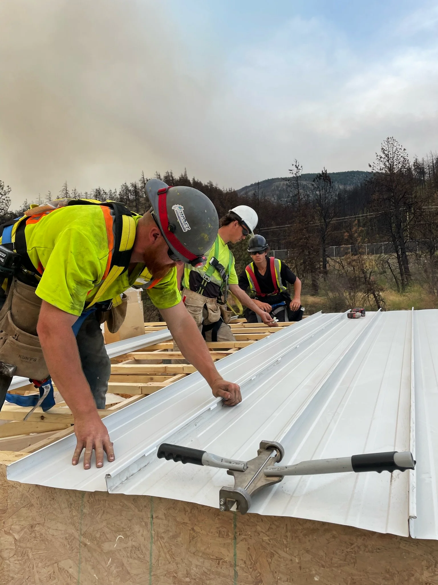 Three construction workers installing a white metal roof panel on a wooden structure.