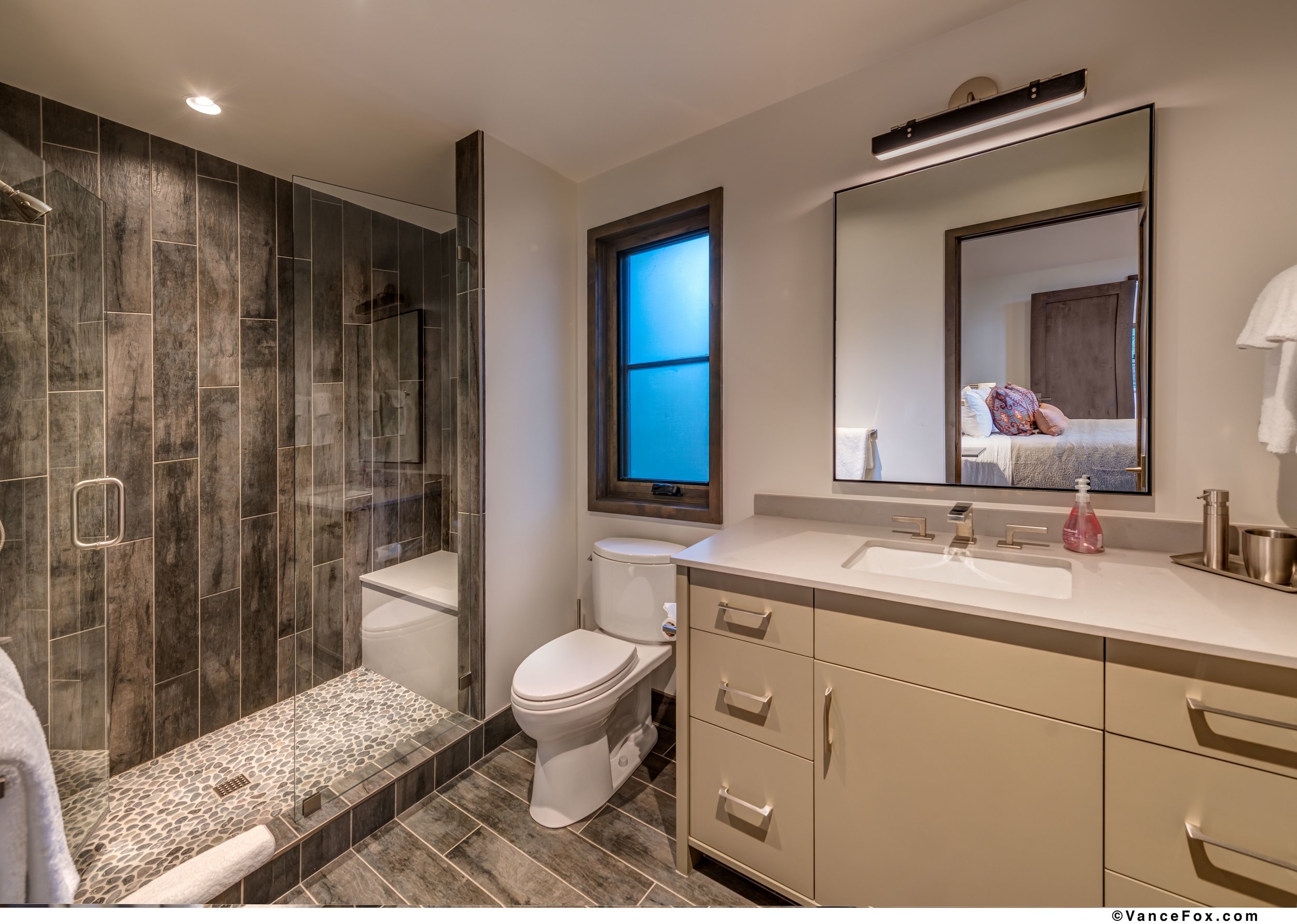 Modern bathroom with walk-in shower, toilet, and vanity with mirror and sink.