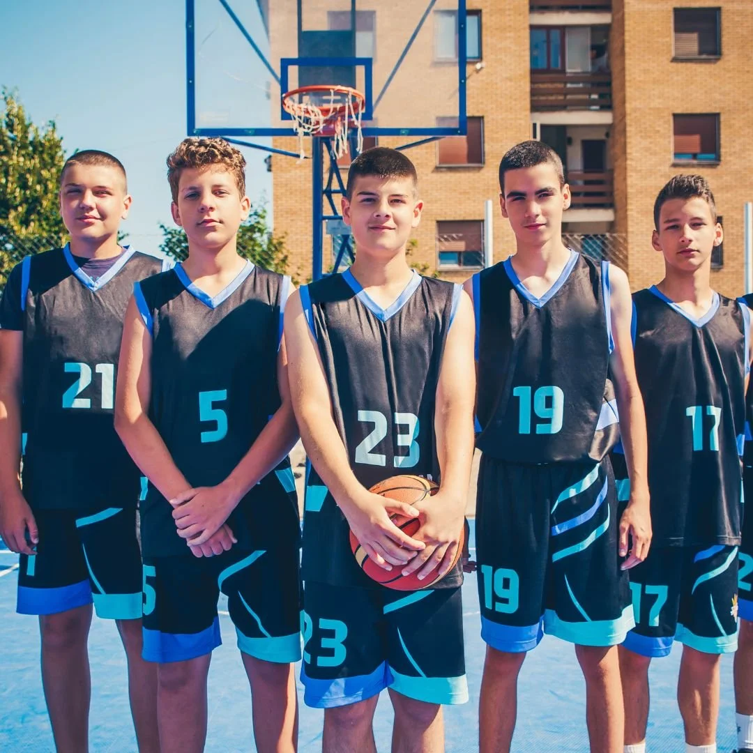 Basketball team posing for a photo in front of a basketball hoop outside