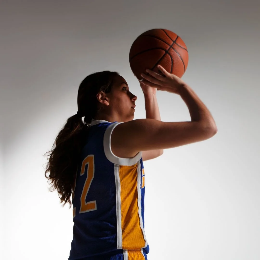 A female basketball player in a blue and yellow jersey prepares to shoot a jump shot 