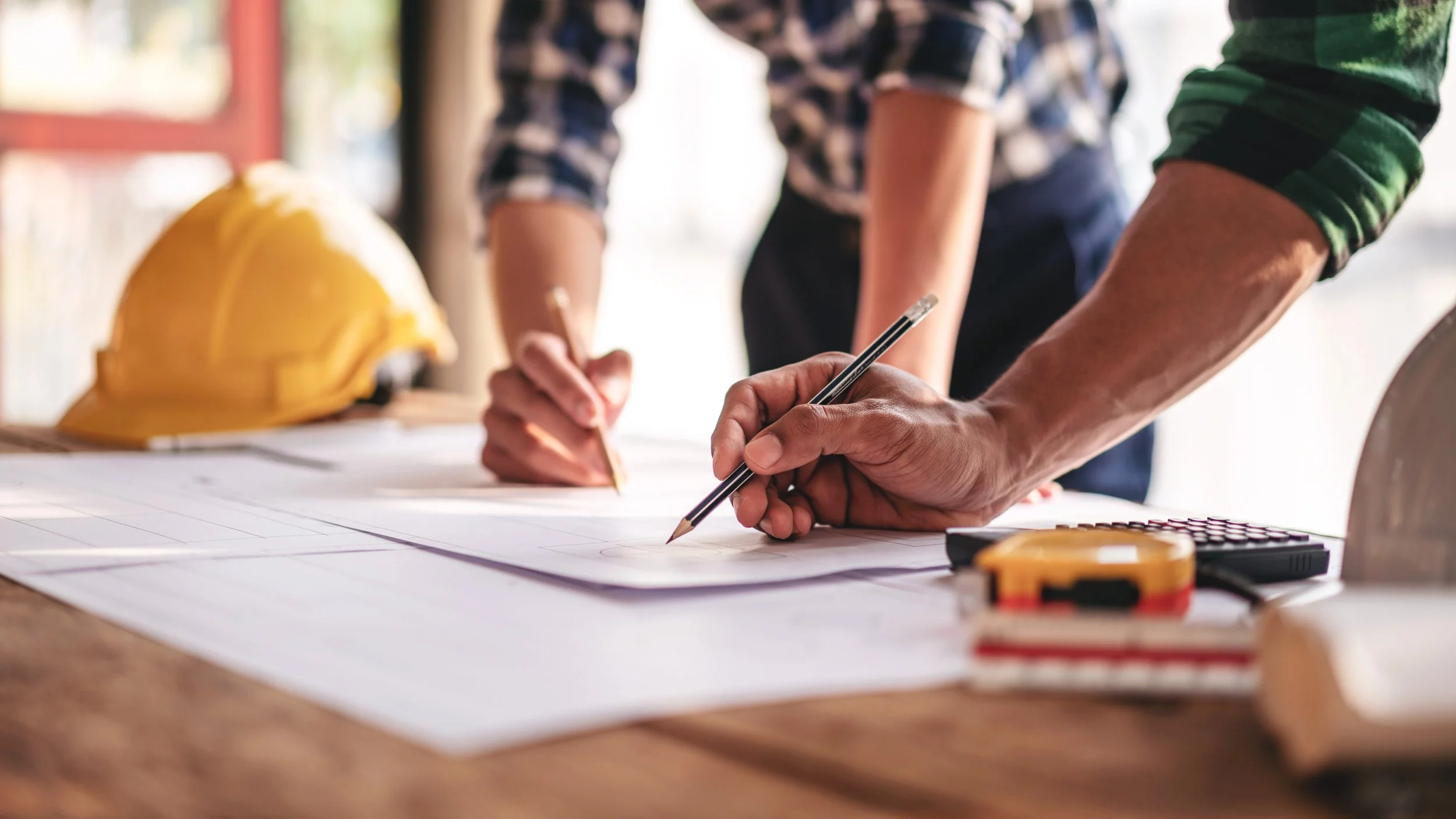 Hands of two men drawing on drafting paper with pencils
