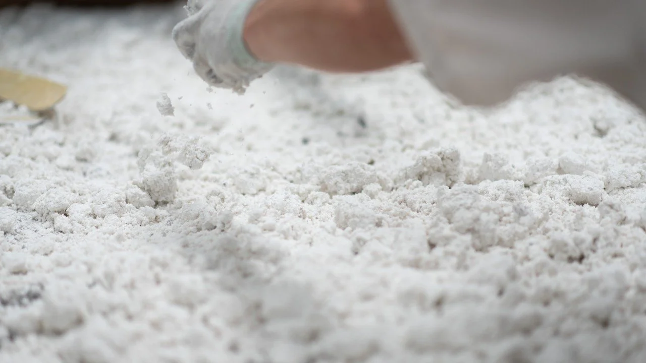 Close-up of a hand wearing a white glove handling white powder, possibly baking or flour, on a flat surface.