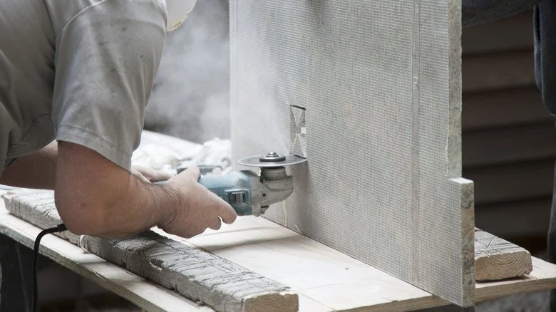A person using a power tool to cut or grind a large sheet of metal on a workbench.